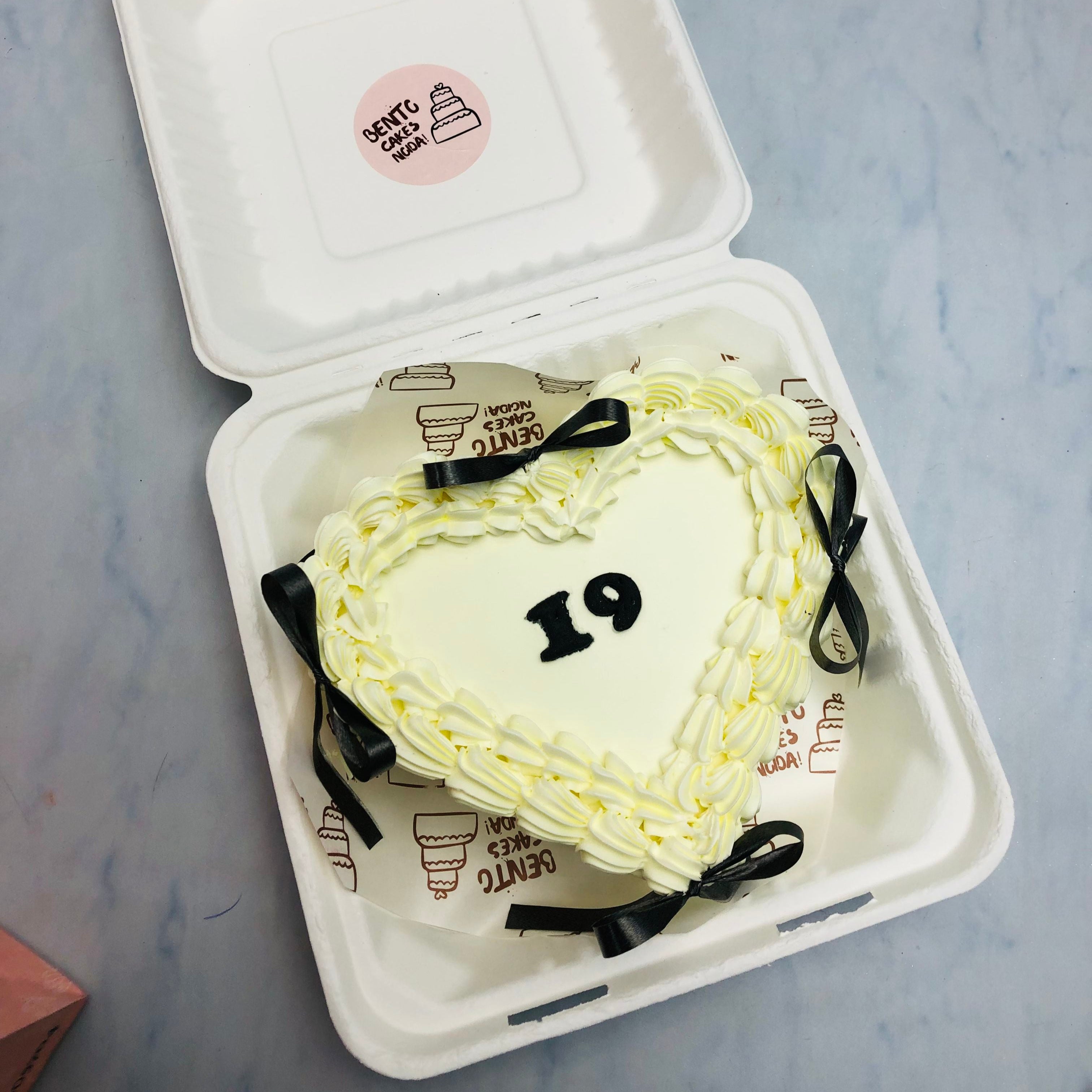 n offwhite heart shape cake with black bow an its surrounding with a year text written on its center.