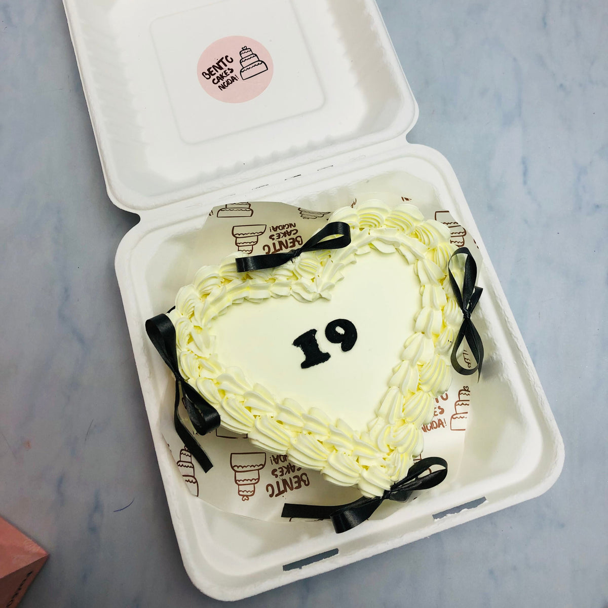 n offwhite heart shape cake with black bow an its surrounding with a year text written on its center.