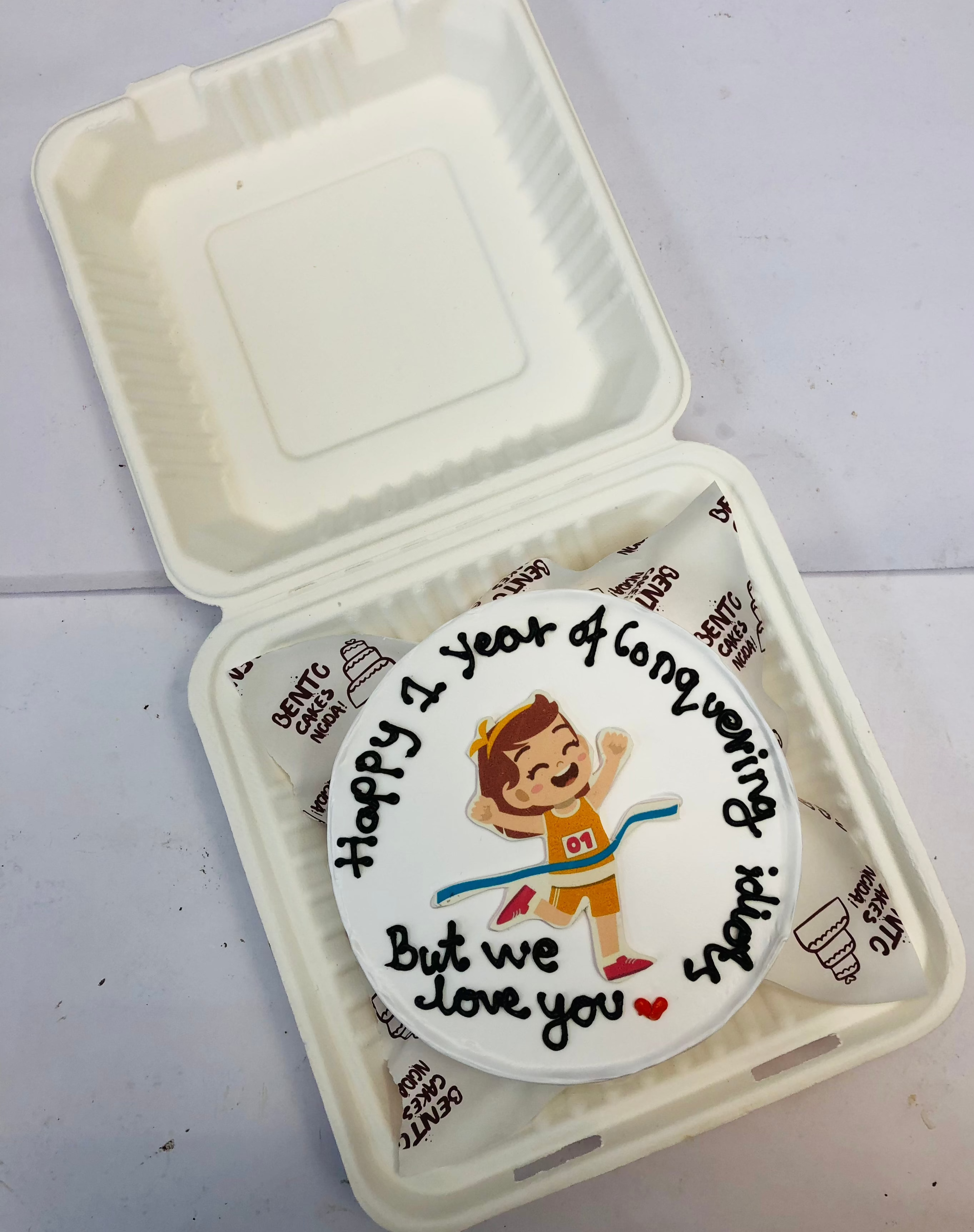 A white bento cake with a race winning boy sticker.