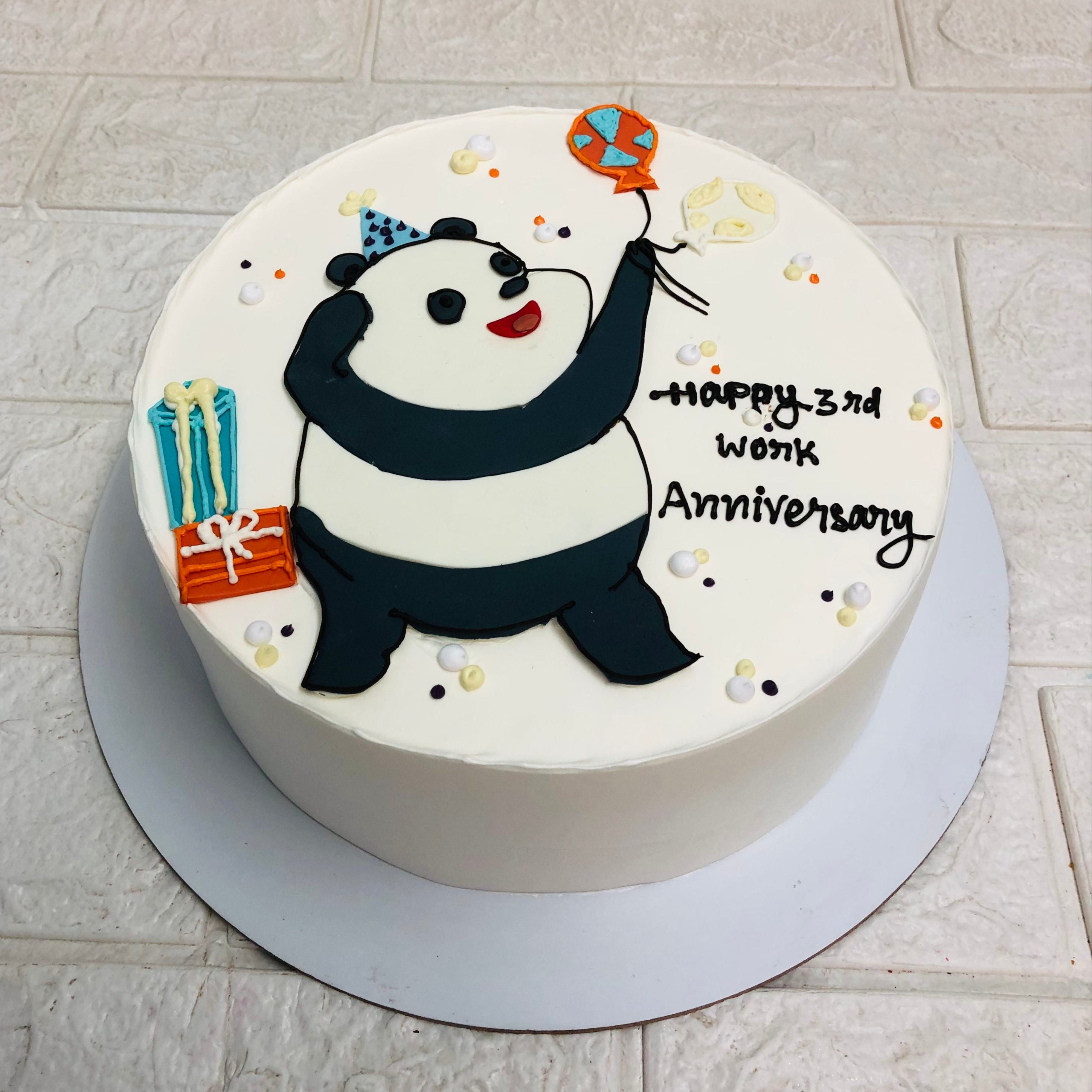 A whimsical cake featuring a panda bear holding colorful balloons, celebrating a joyful anniversary with a cheerful message.