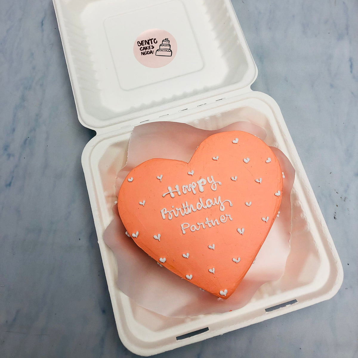 A peach color heart shape cake with white hearts design all around the cake.