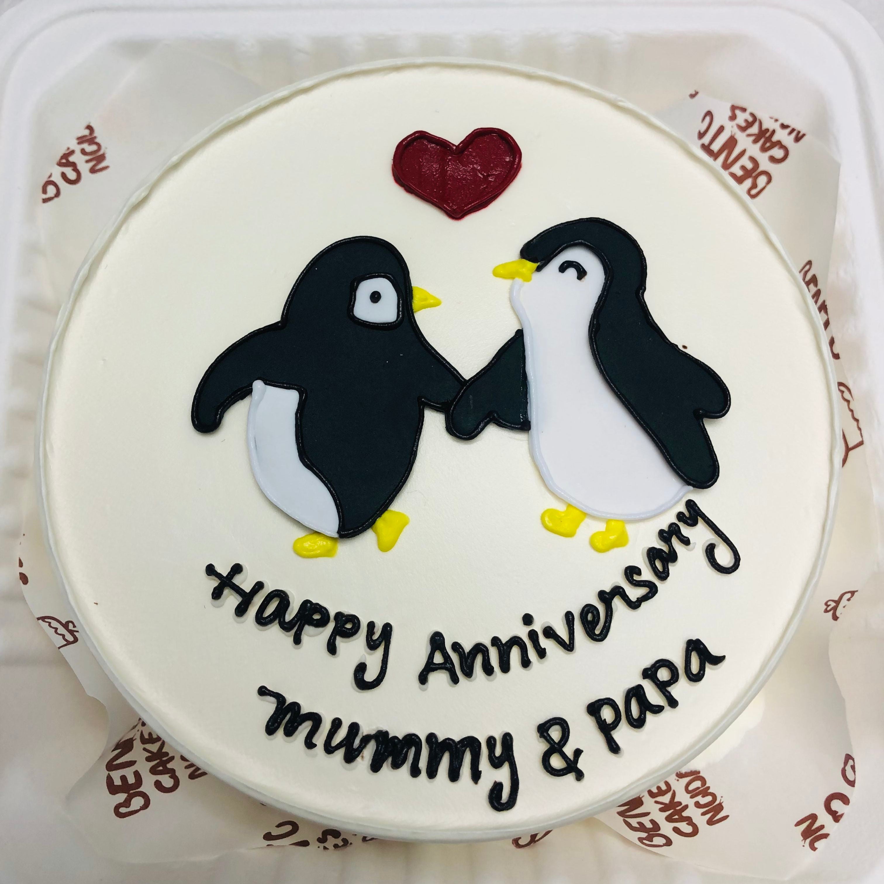 A delightful penguin-themed cake celebrating a happy anniversary, adorned with festive decorations and a joyful design with front view.