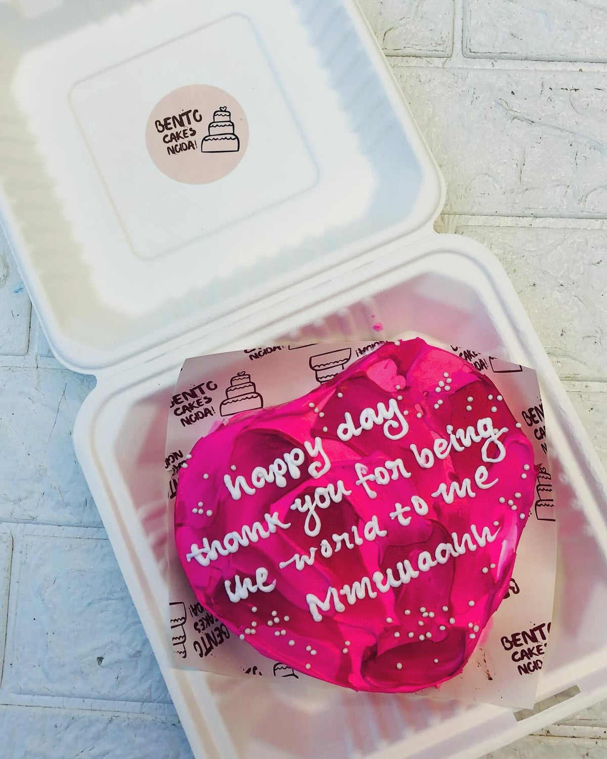 A dark pink heart bento cake with pink shads design on it and loving text with white icing written on it.