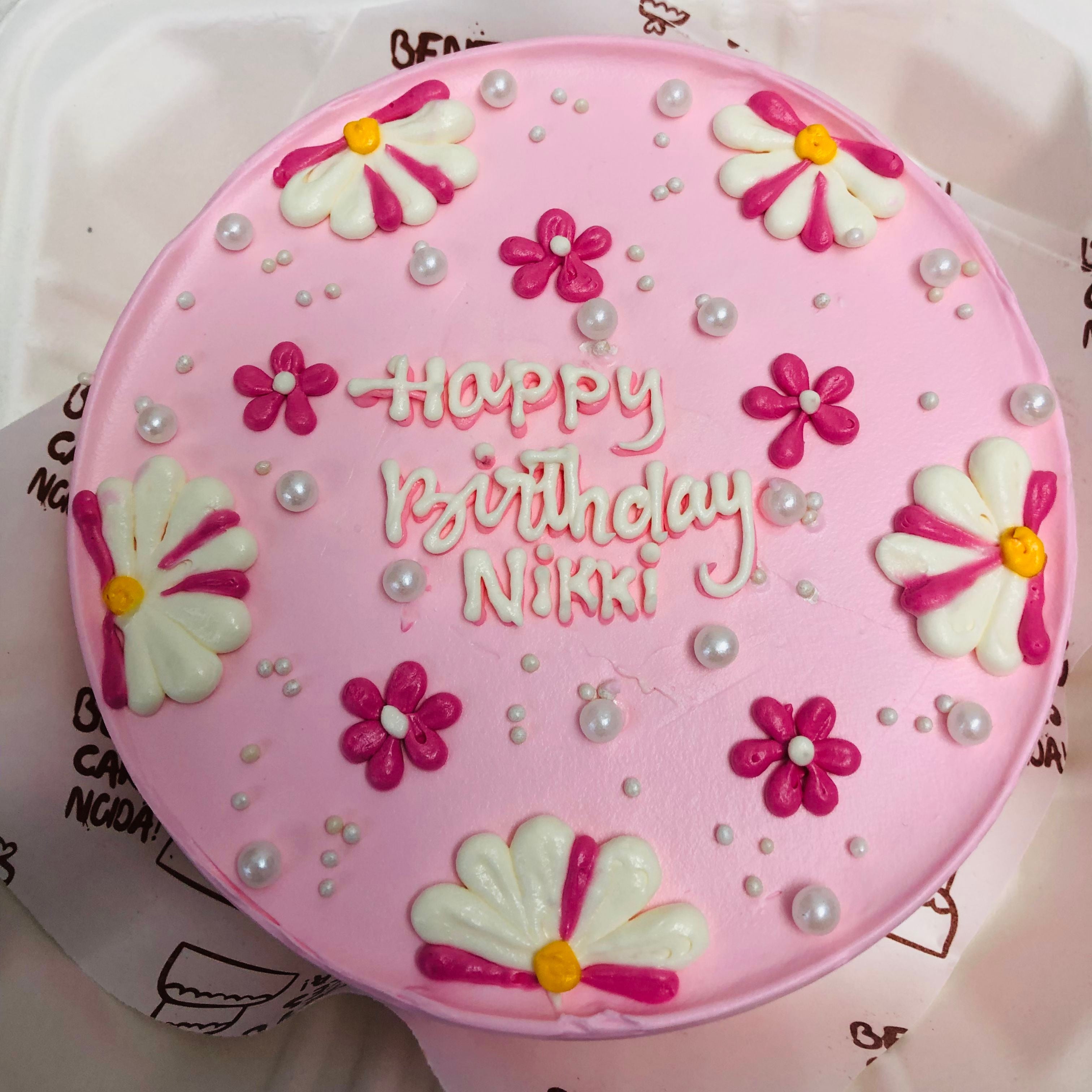 A beautifully crafted pink bento cake featuring floral decorations and the message 'Happy Birthday Nikki.