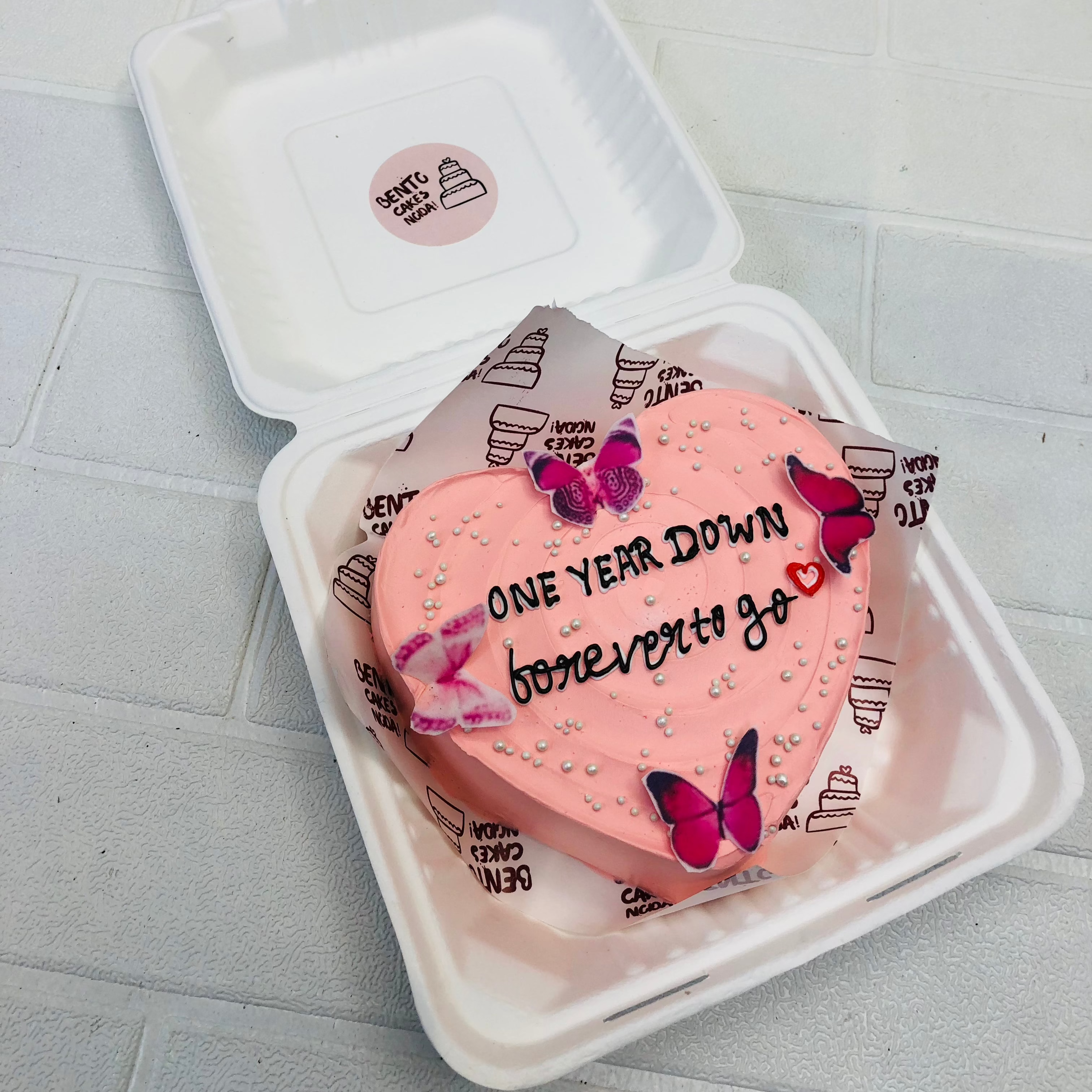 A butterfly theme 1stb anniversary cake in hearts shape design and decorated with pink butterflies on.