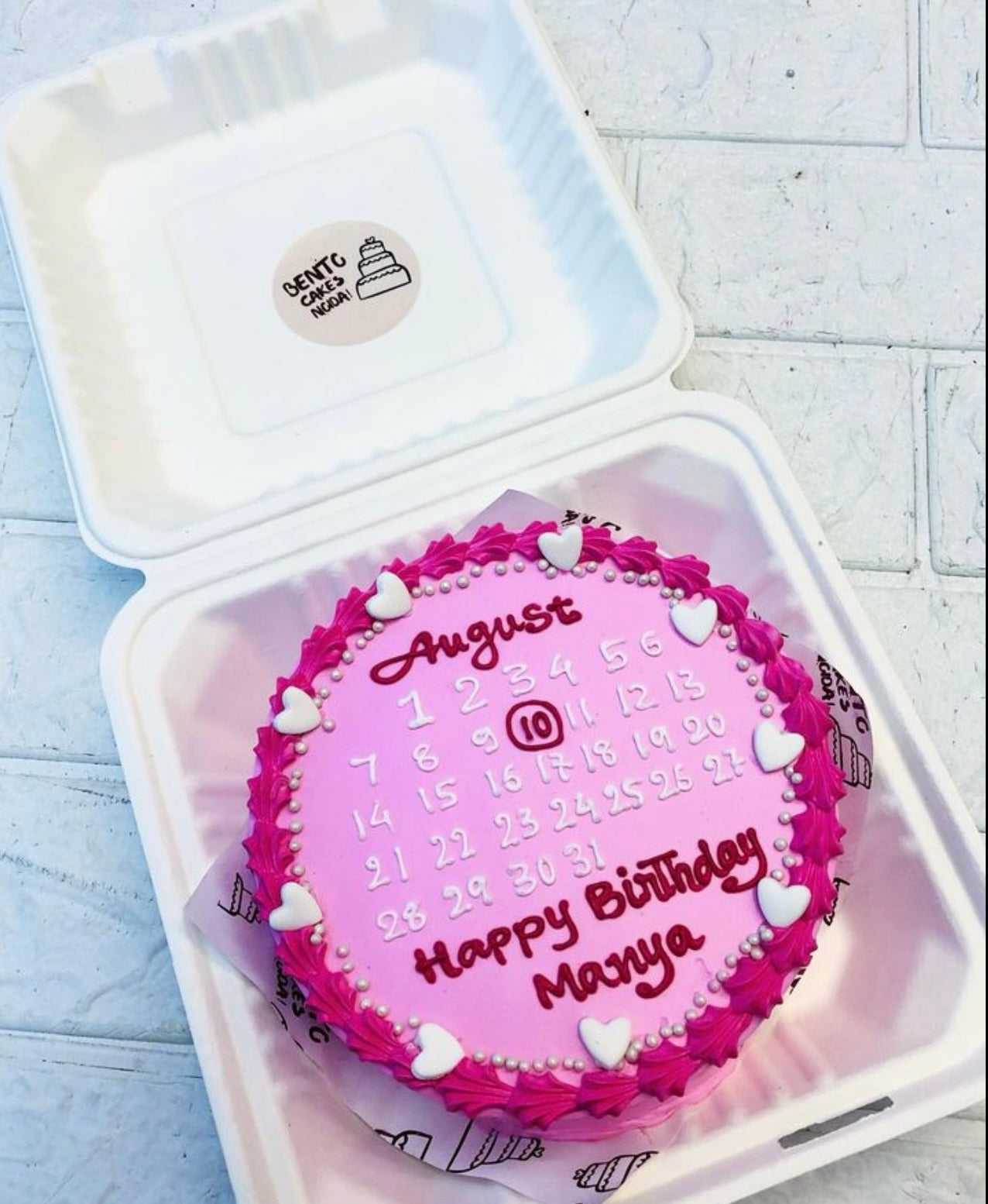 A light pink bento cake with white calendar design and decorated with pink truffle on boundary.