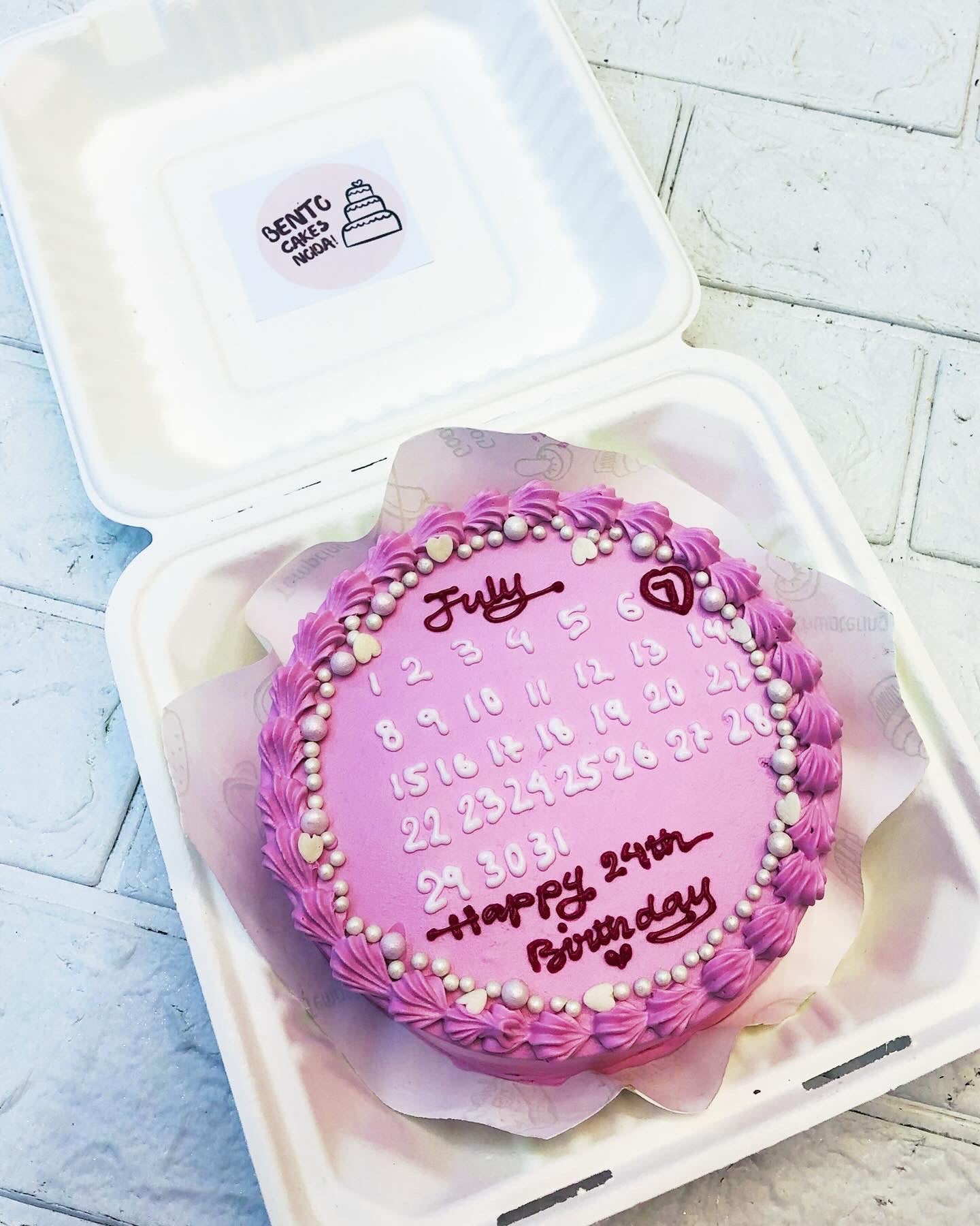 A pink designer bento cake with calendar theme for birthday occasion.