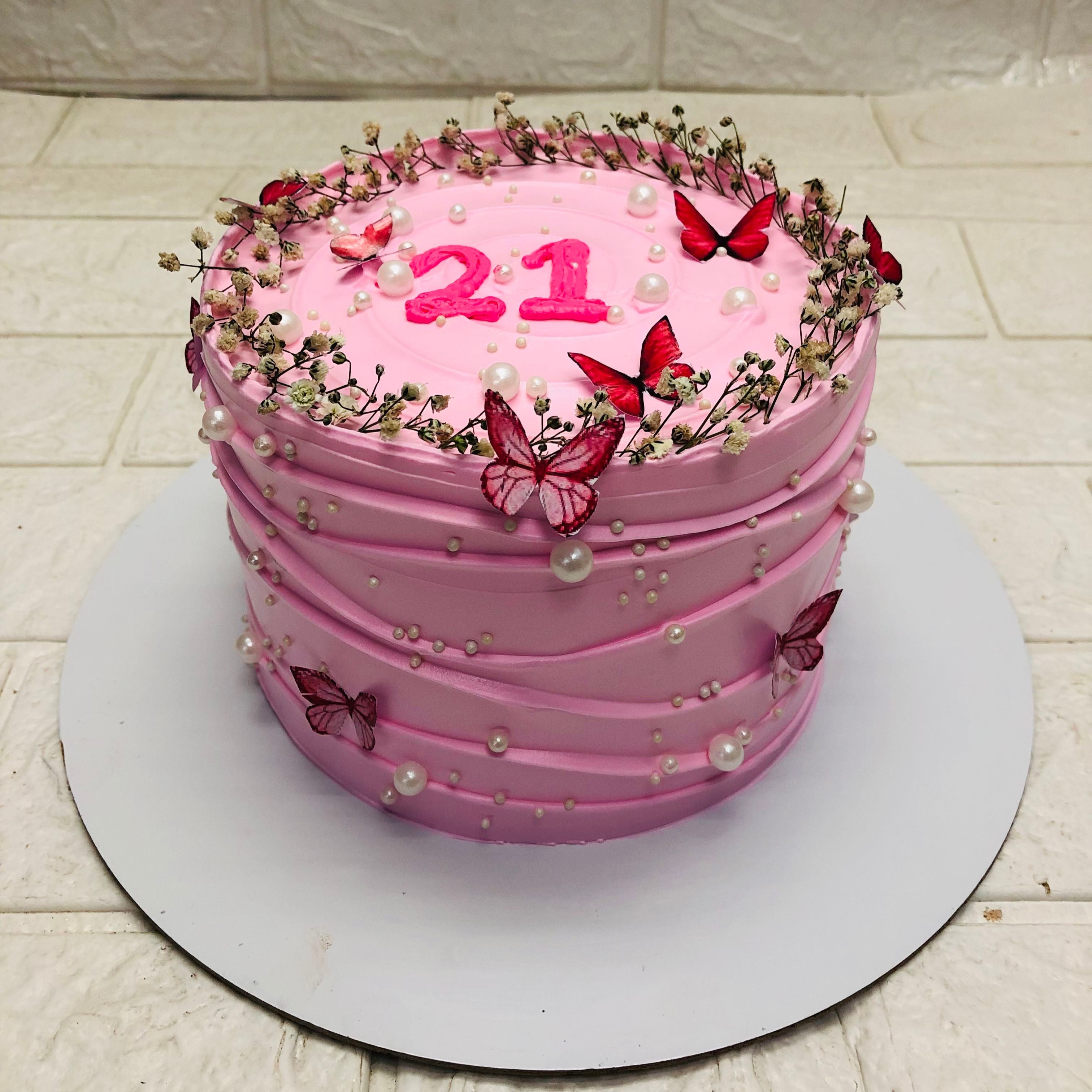 A pink cake adorned with butterflies and topped with the number 21, celebrating a special birthday occasion.