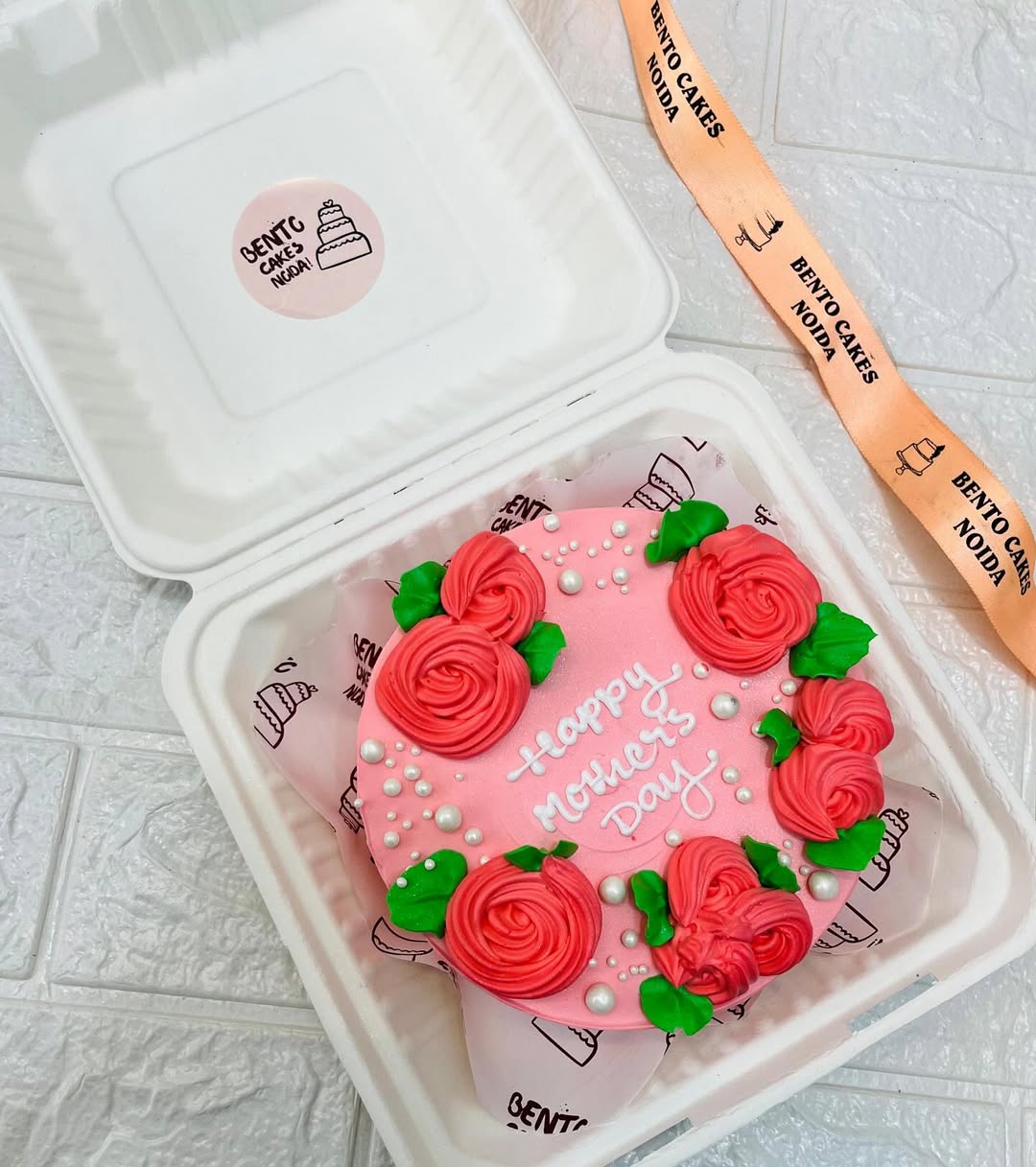 A light pink cake with pink floral design with leafs and a "Happy Mother's Day" text written on it.