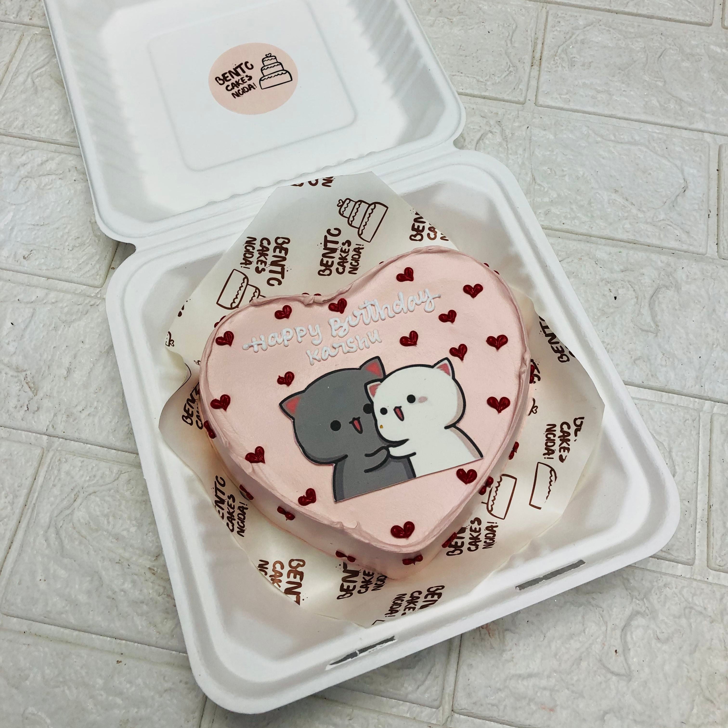 A pink heart shaped cakes adorn with cute bubu dudu cartoon sticker and a text "Happy 2 Years" written with black icing and decorated with pretty red hearts.