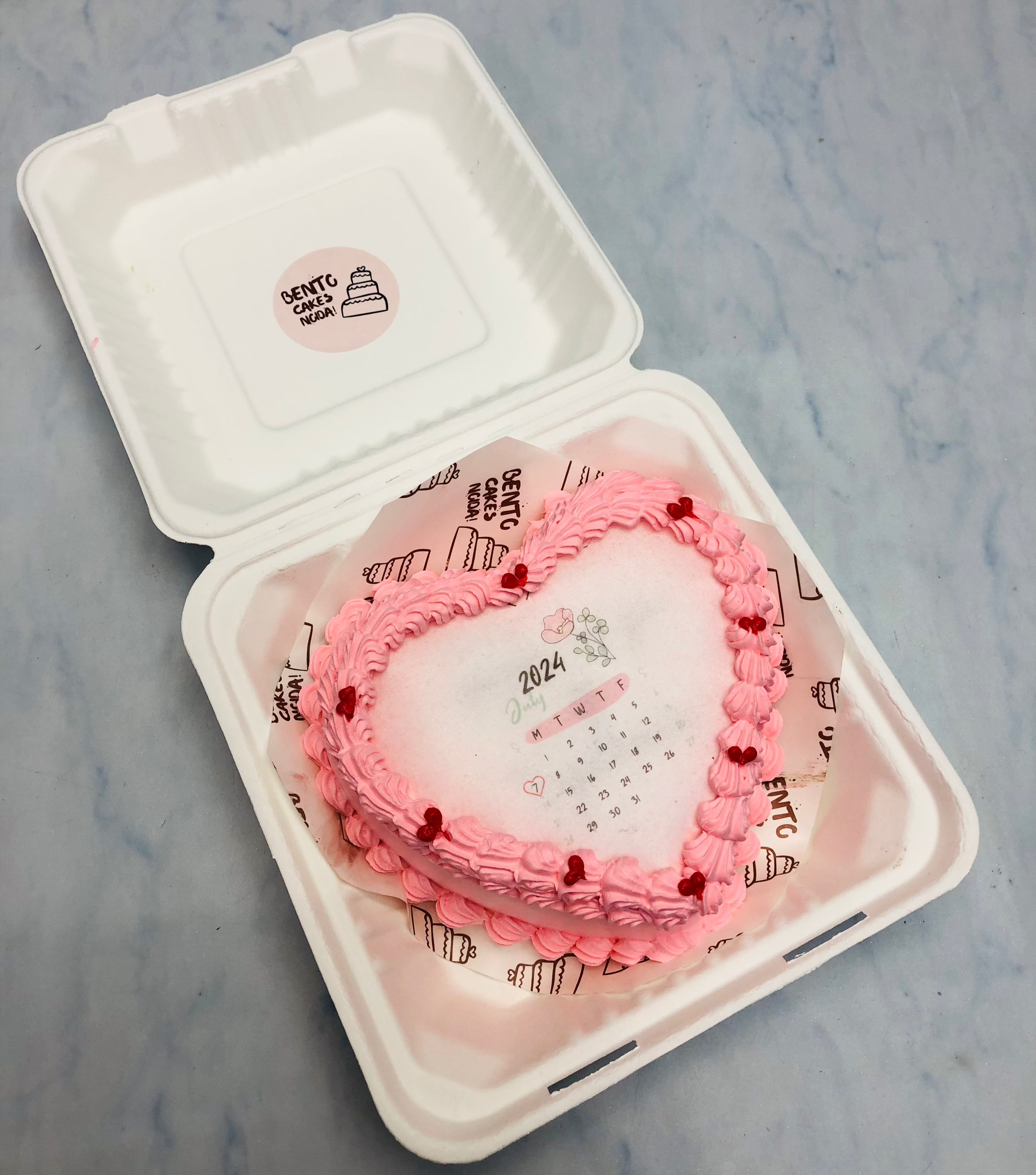 A light pink heart shape fire bento cake with calendar design for birthday.