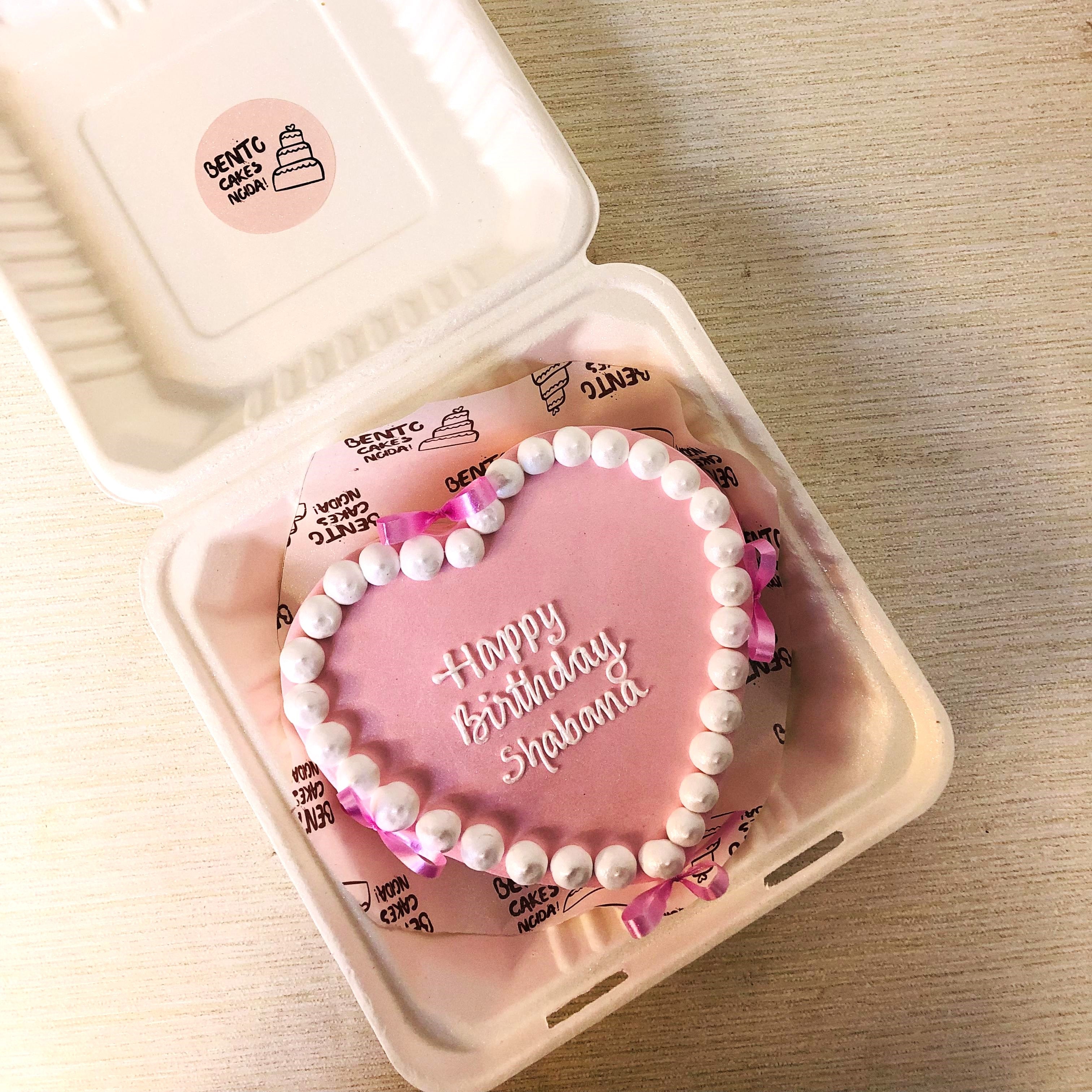 A light pink cake with heart shape design and decorated with pink bows.