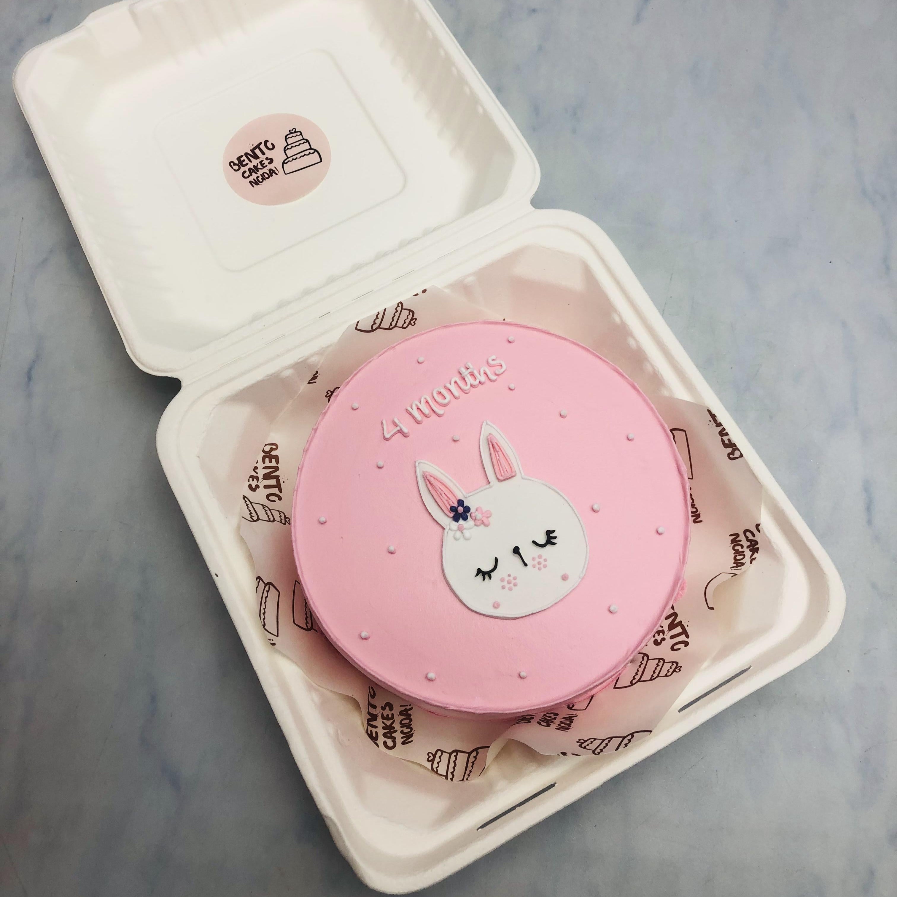 A light pink cake designed for baby girl, having a cte rabbit face with 4 months text.