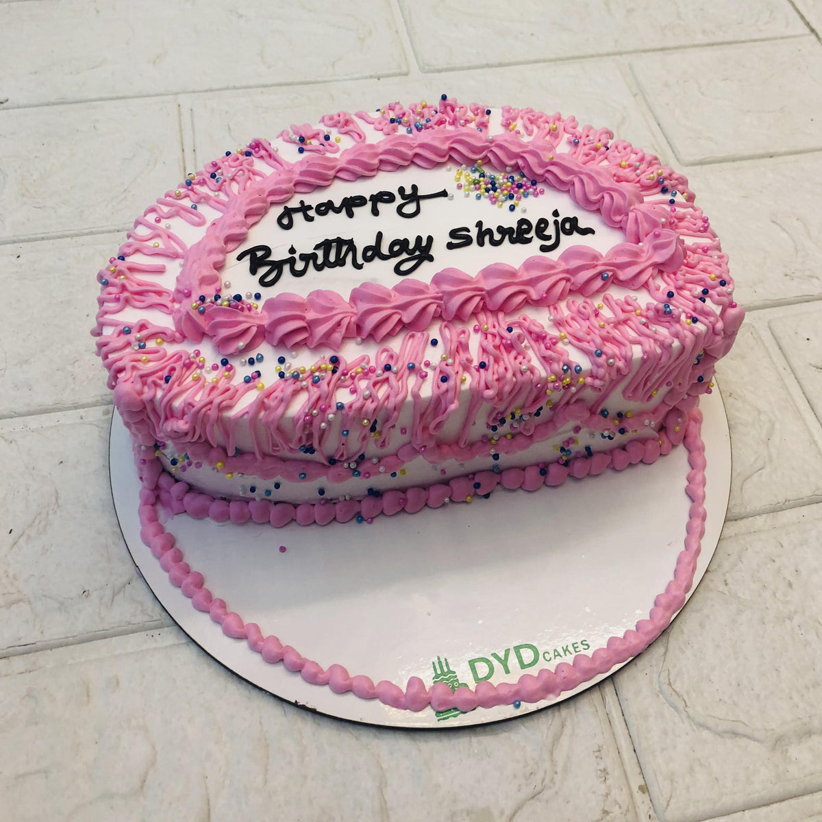 A birthday cake adorned with pink icing and colorful sprinkles in a half shape design, celebrating a joyful occasion.