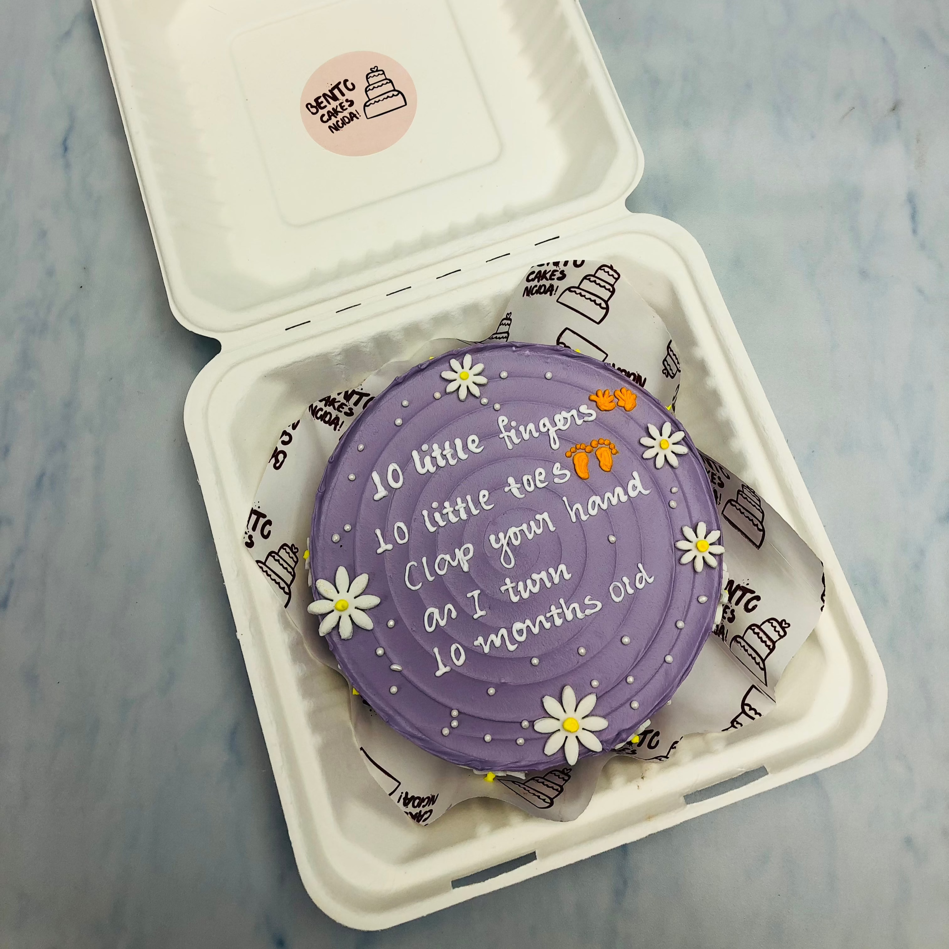A pretty purple bento cake with a english poem written on it and decorated with white florals and sprinkles.