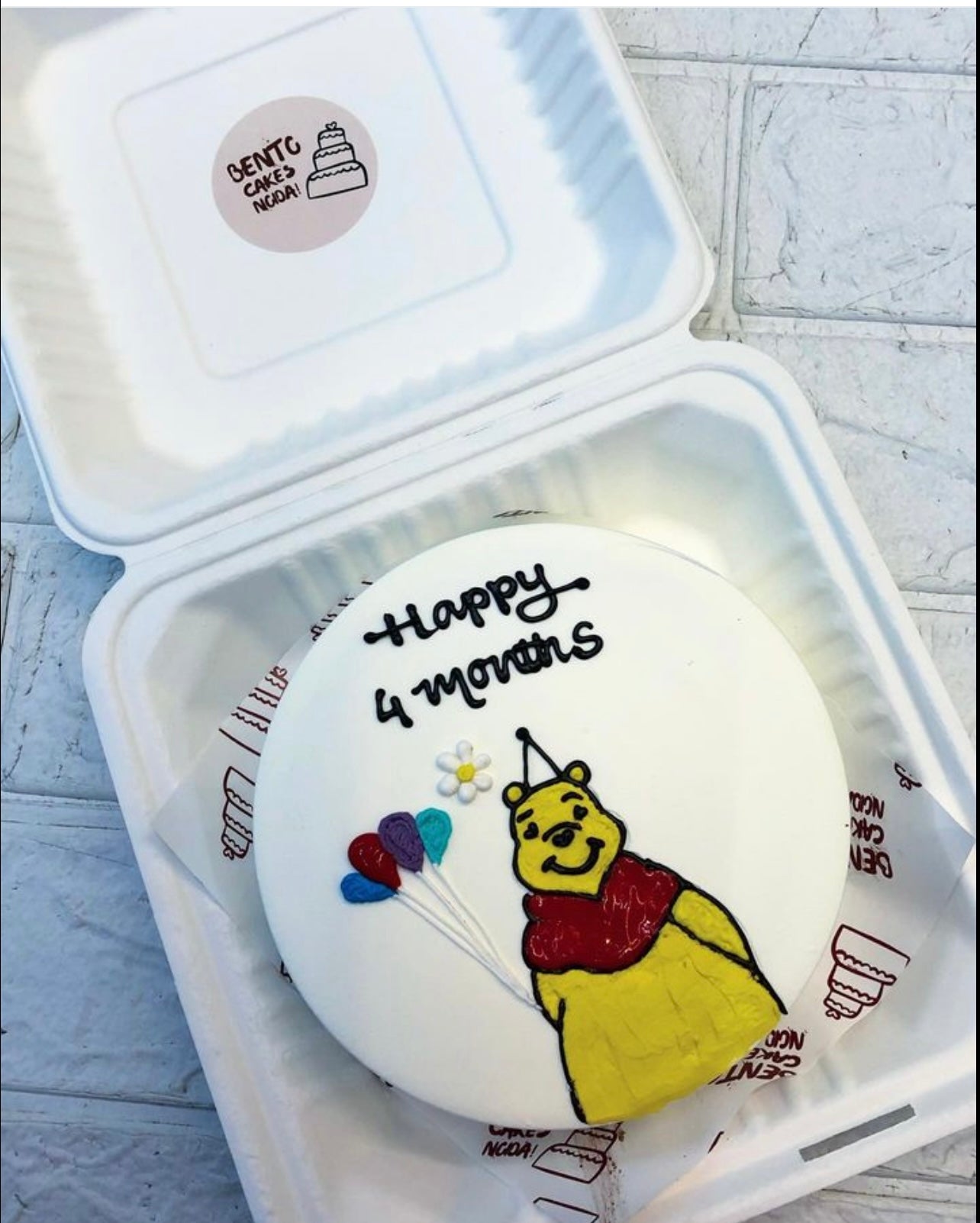 A white bento cake with winny the pooh carton charater bear mae for 4 months baby.