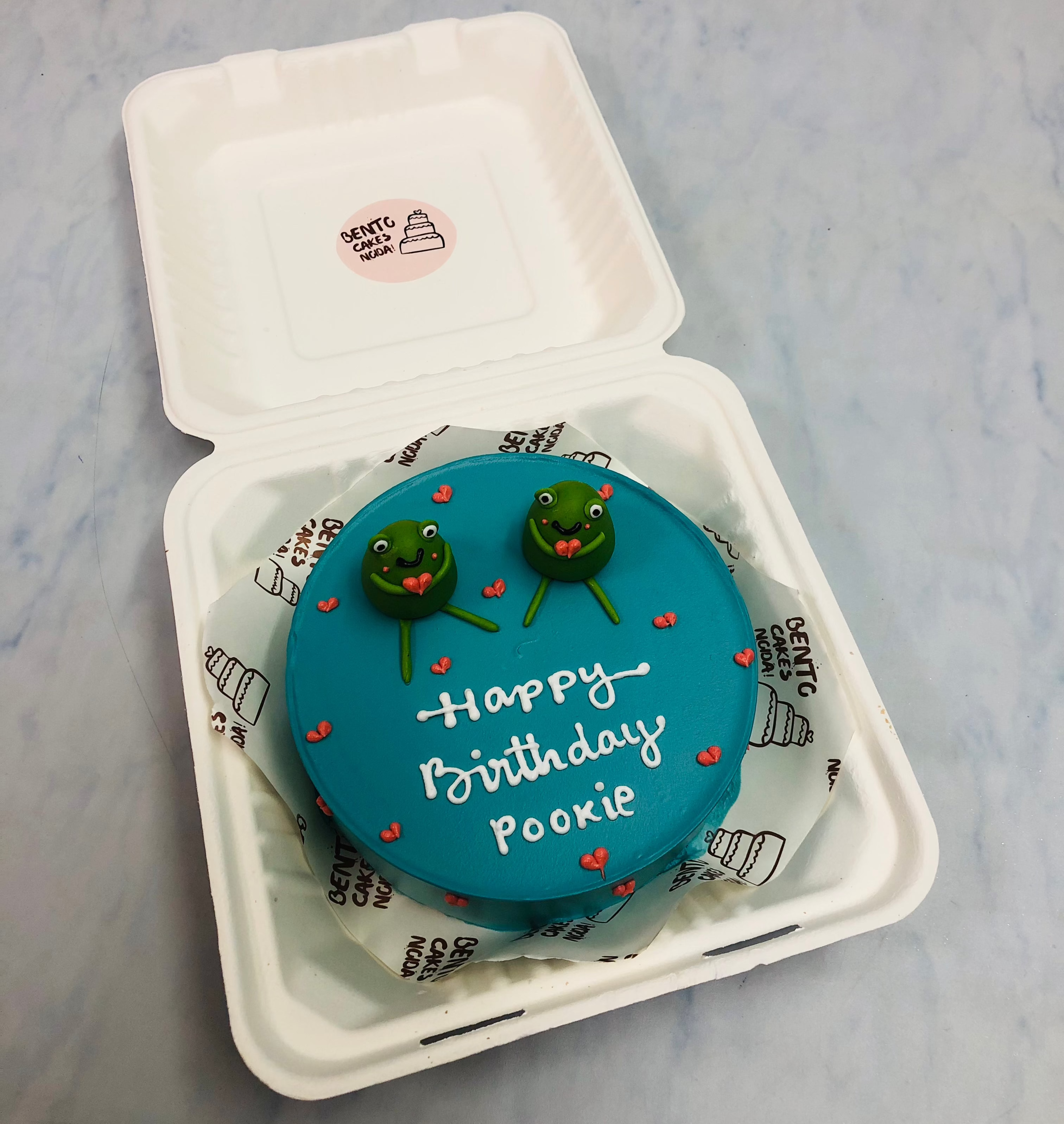 A shiney blue bento cake with tow fondant cartoon characters celebrationg birthday.