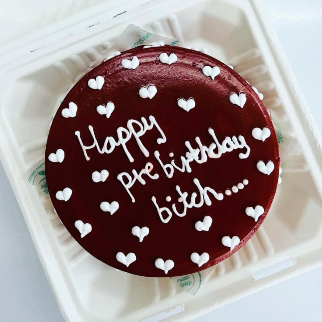A chocolate cake adorned with "Happy Pre Birthday Bitch" written in elegant icing, celebrating a special occasion.