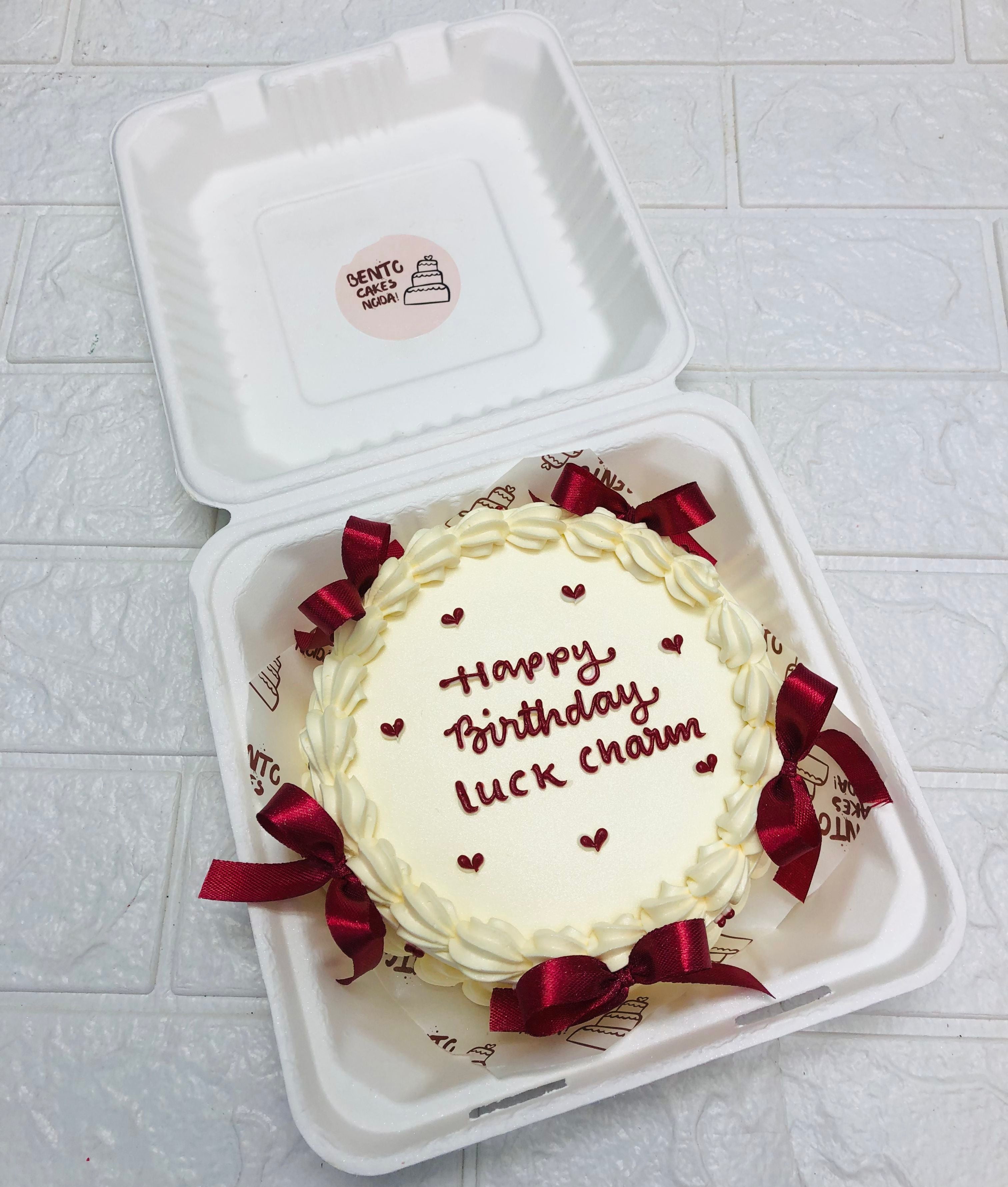 An off white bento cake decorated with red bows and little red hearts for birthday.