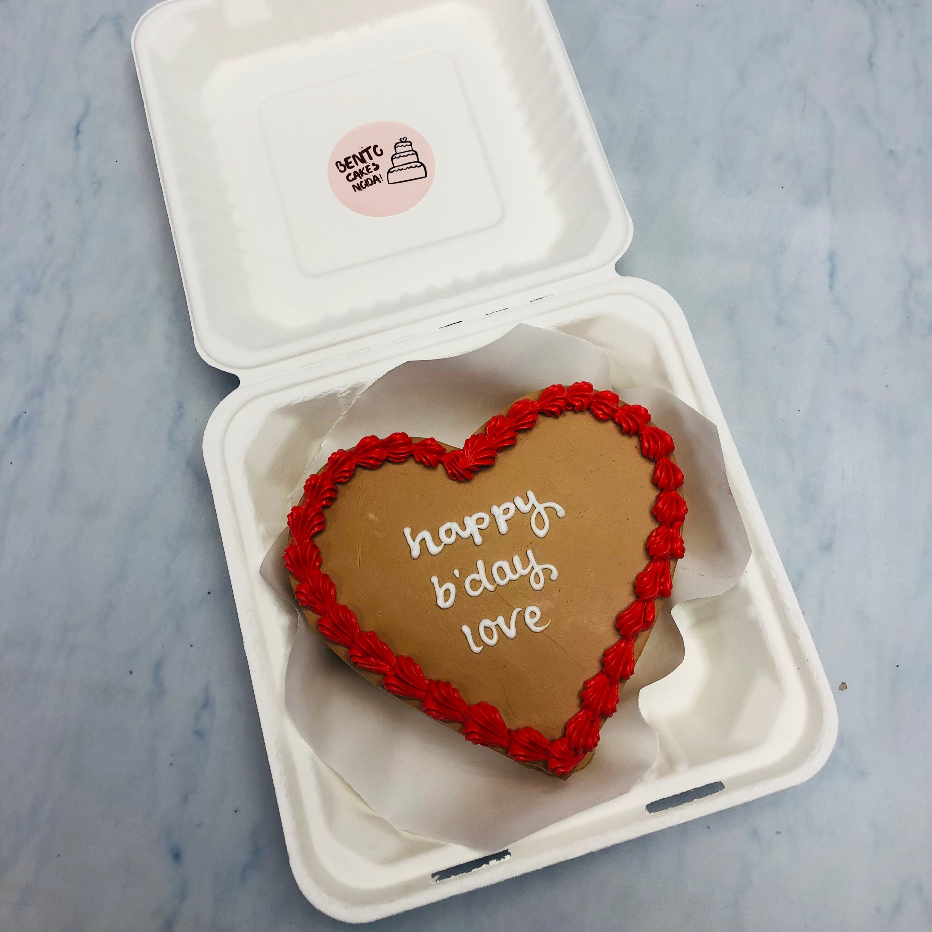 A pretty brown heart bento cake with red floral design on its boundary and a "happy b'day love" text on it.
