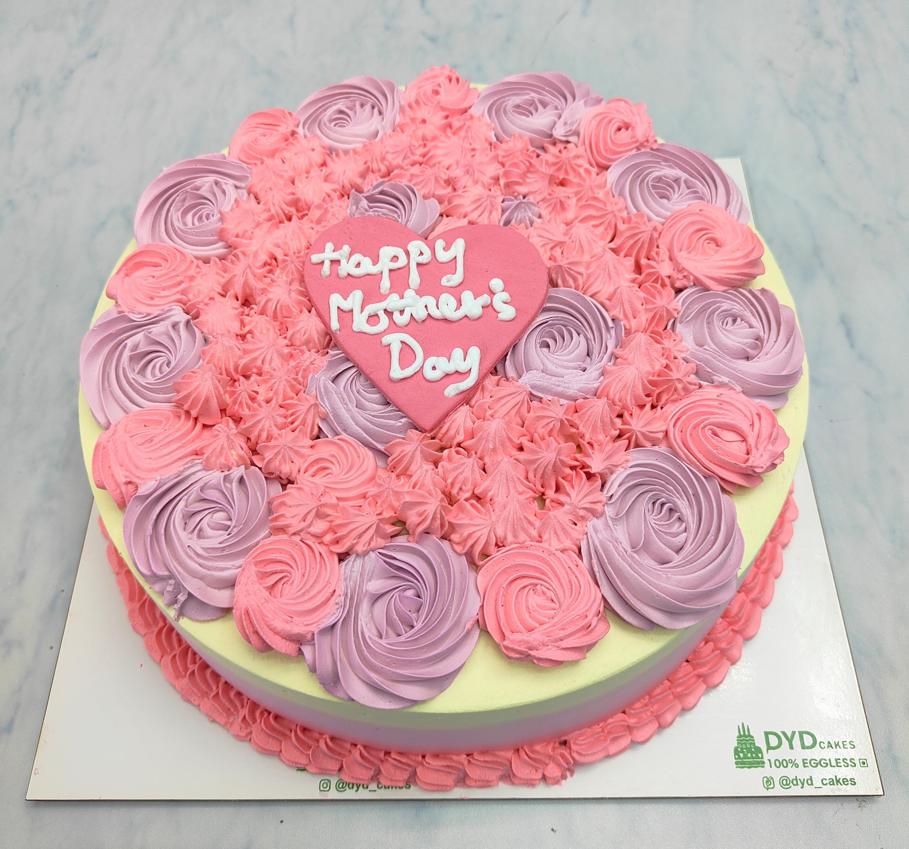 A dual color cake with pink and purple floral design and a "Happy Mother's Day" text written in fondant heart design.