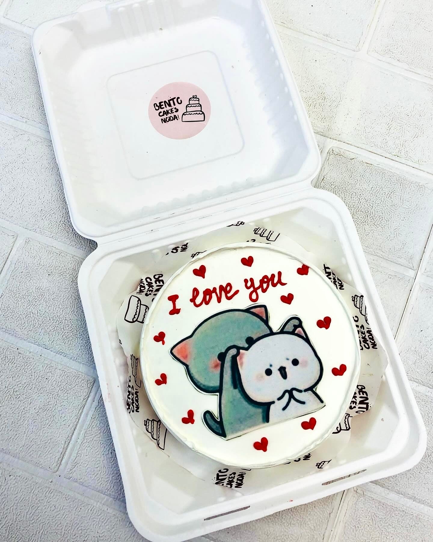 A white bento cake having grey white bubu dudu cartoon print, desoated with little red hearts.