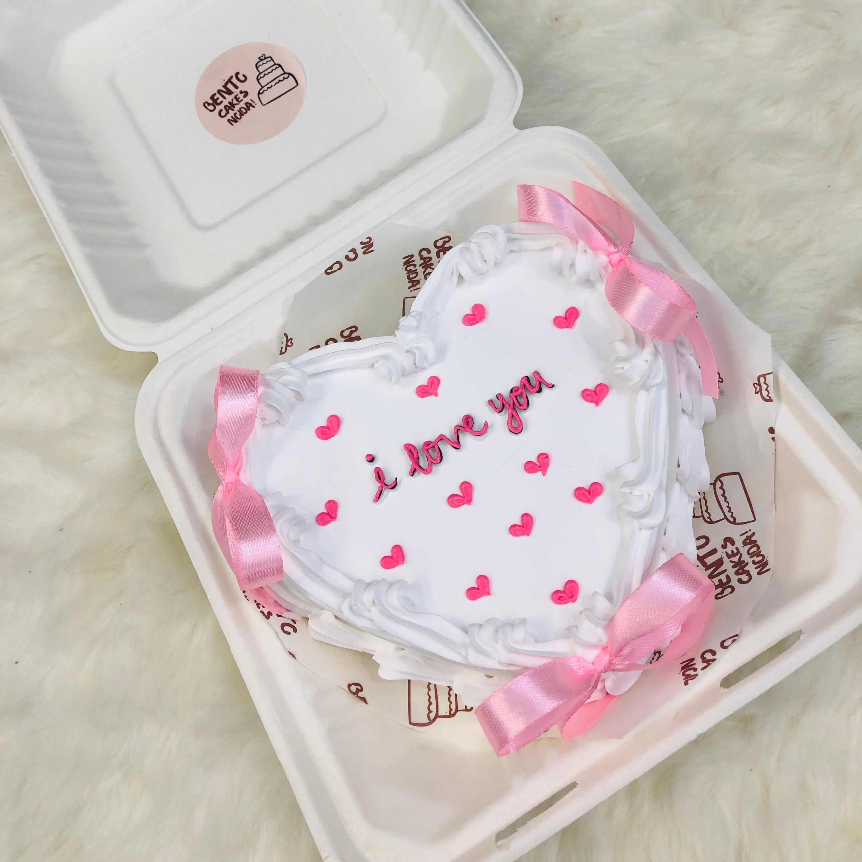 A heart-shaped cake elegantly presented in a bento box adorned with a pink ribbon, perfect for a special occasion.