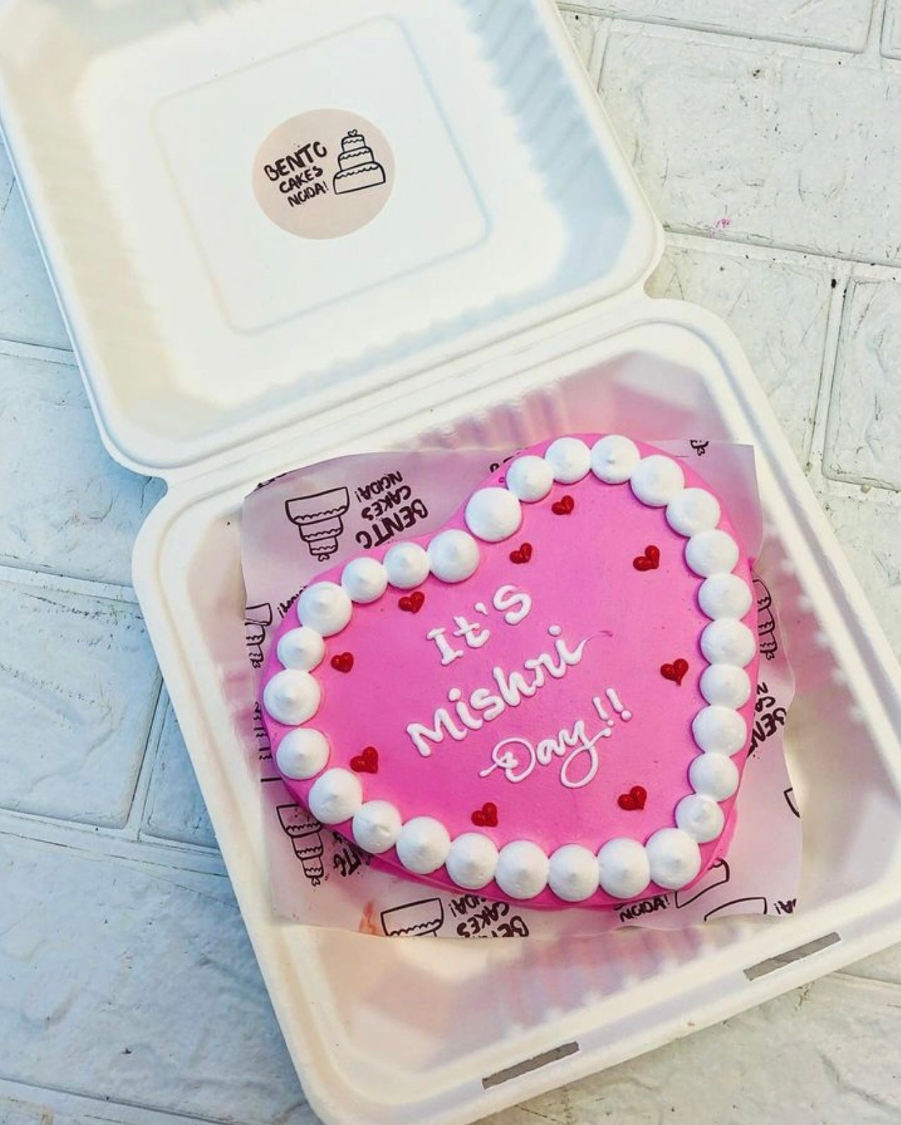 A baby pink color heart shape cake with white tuffles on its surrounding with a beautiful text.