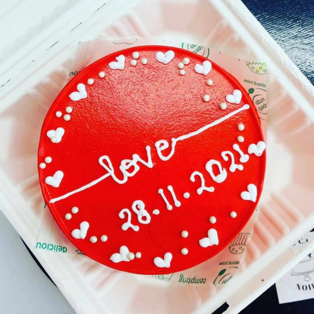 A red and white heart-shaped cookie displayed in a clear plastic container, showcasing its vibrant colors and design.