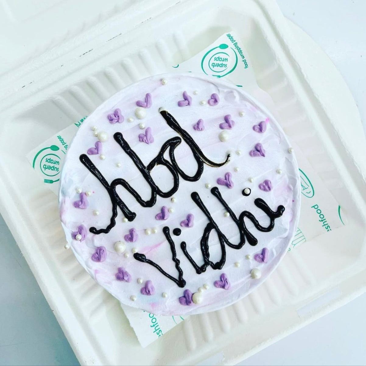 A white box containing a beautifully decorated purple and white cake, showcasing an elegant dessert presentation.
