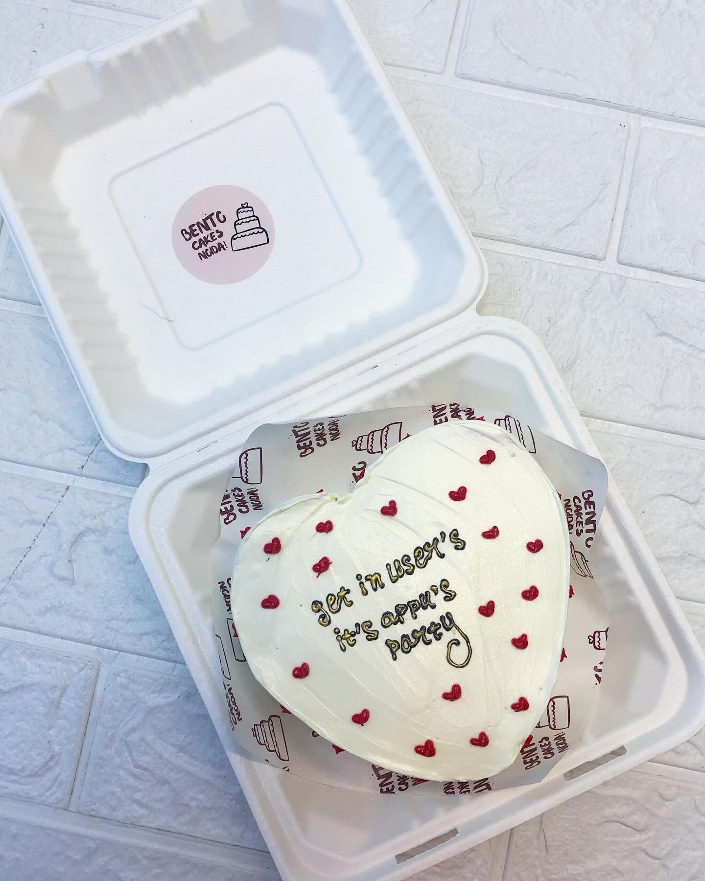 A white hearts bento cake with cute red hears design and a text written with golden icing on it.