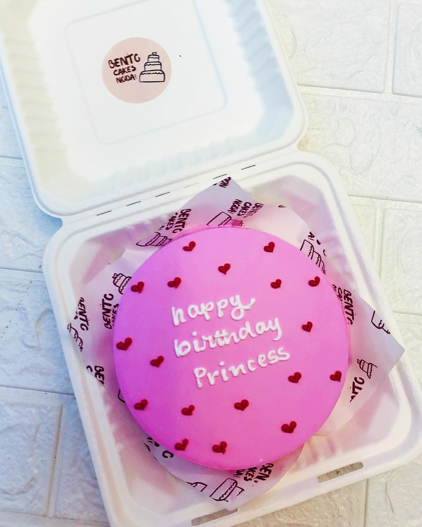 A pink frosting bento cake having red hearts design and a text written with white icing.