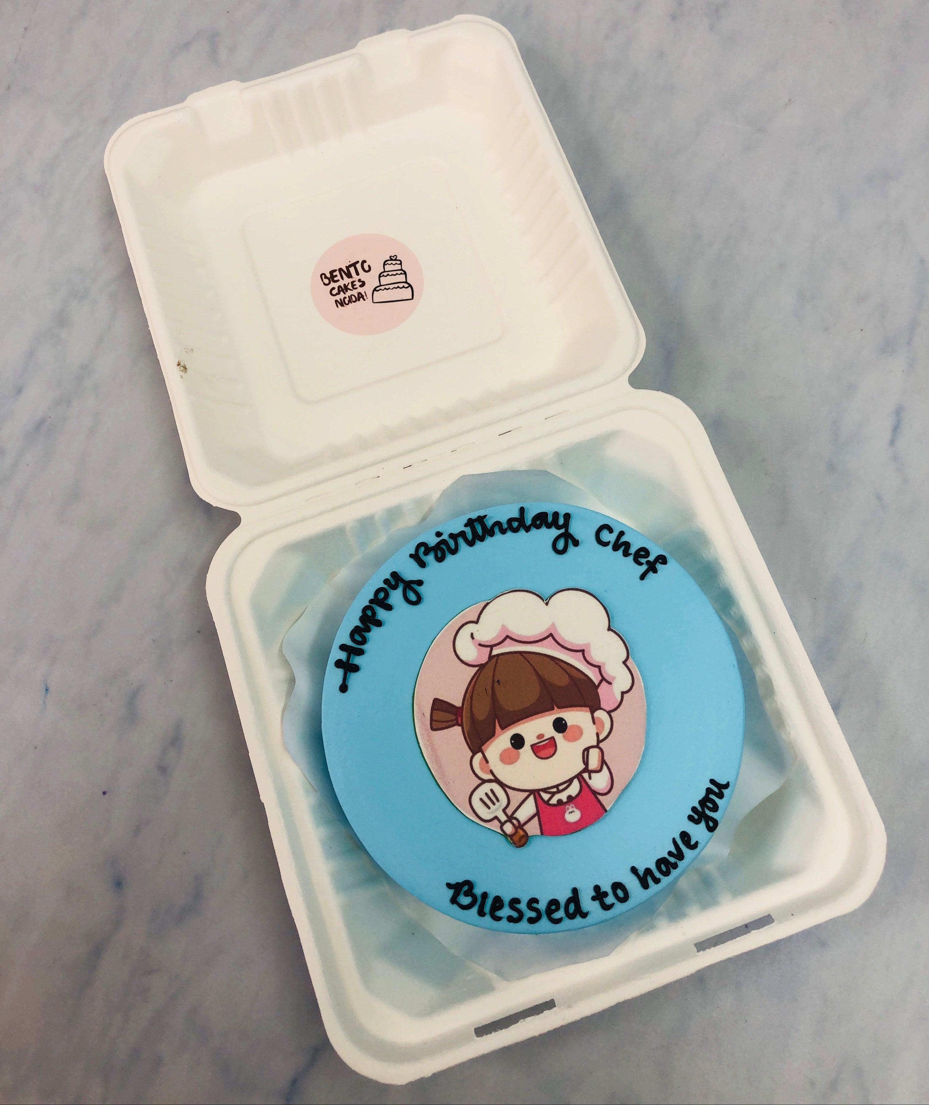 A skyblue bento cake having a chef girl print and is designed for her birthday.
