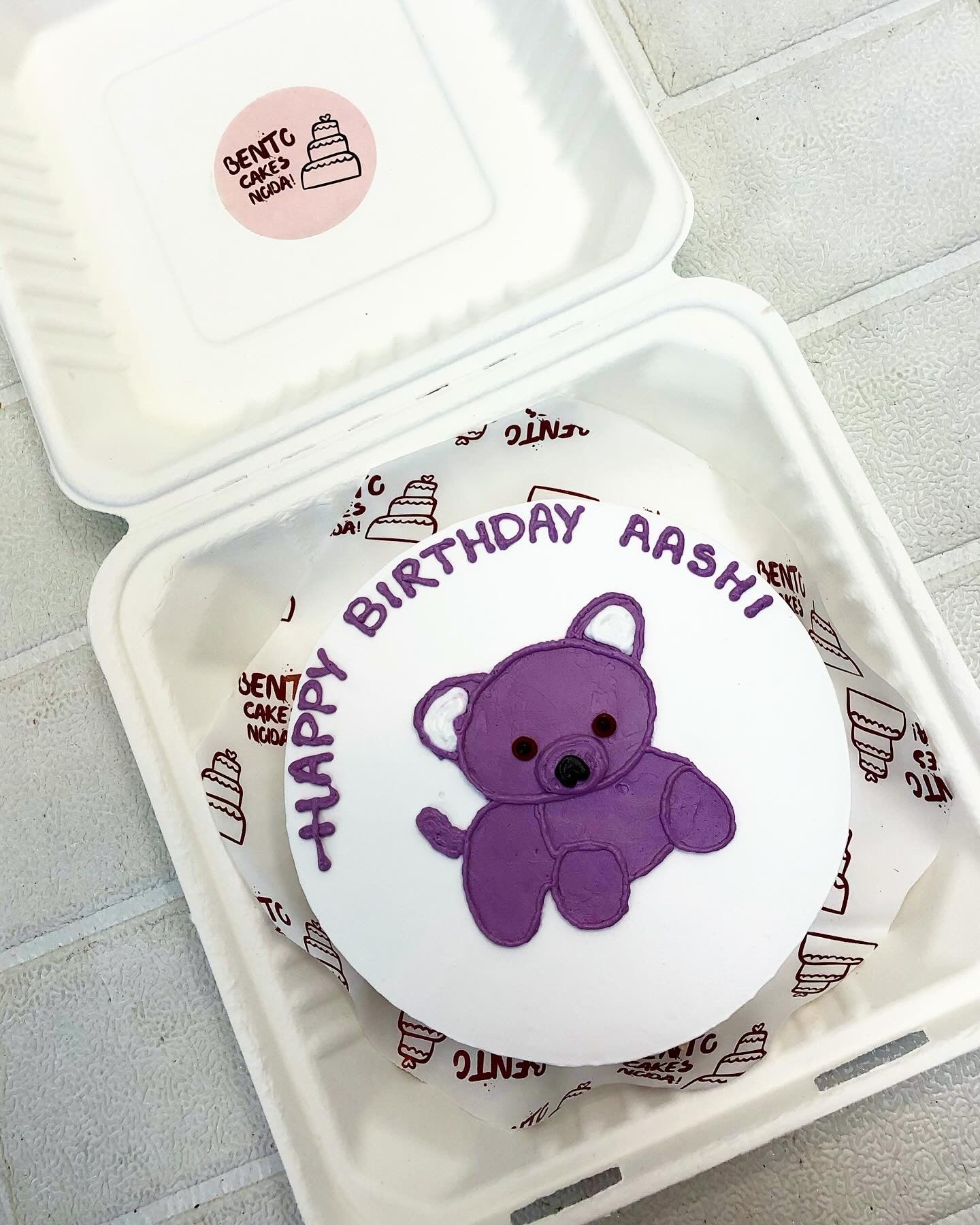A white bento cake with cute purple Teddy and text written with purple color.
