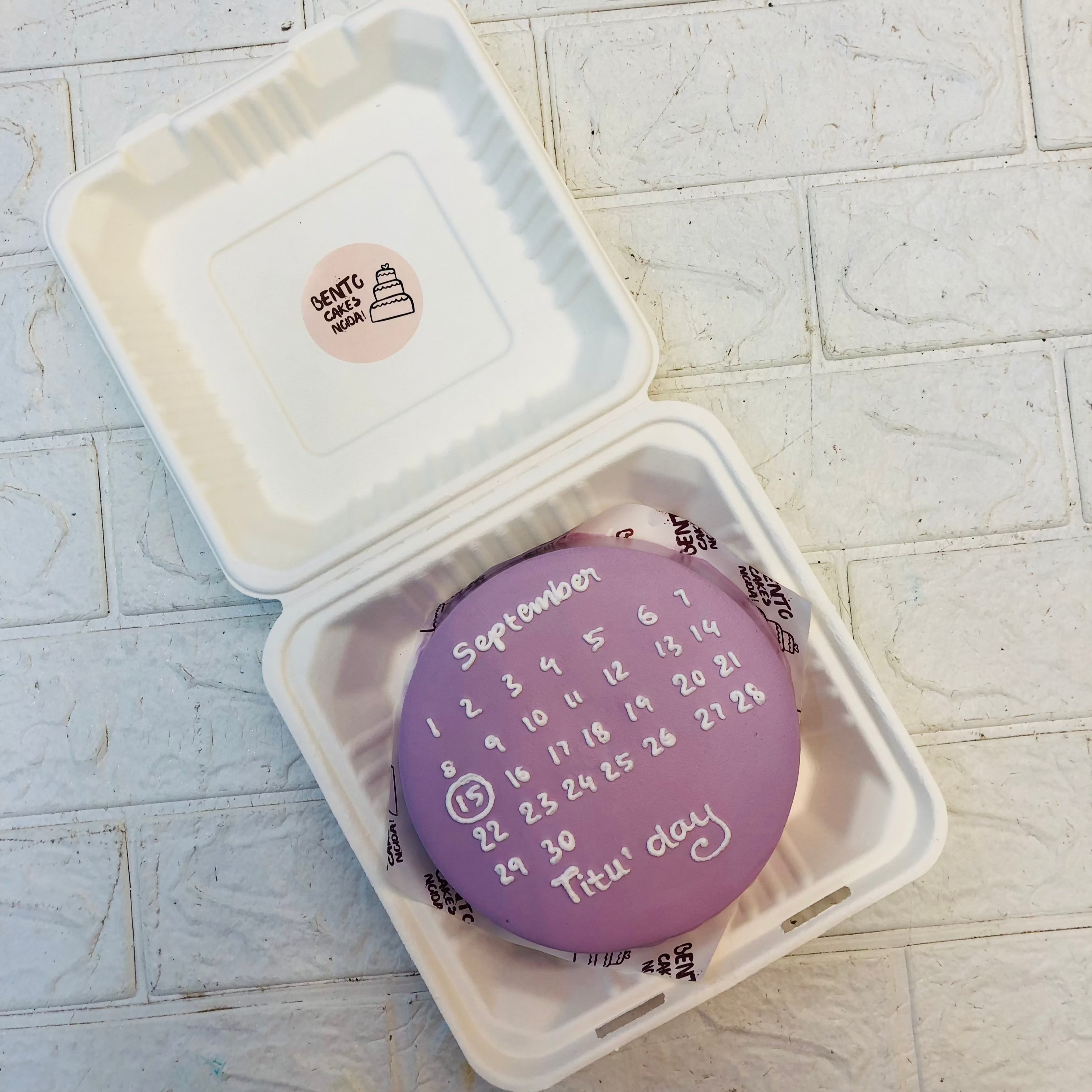A purple bento cake with white calendar month design on it.