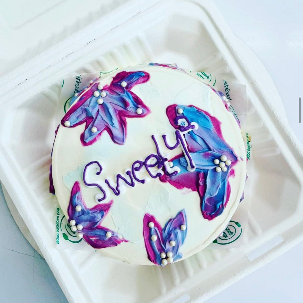 A cake featuring delicate purple floral design, carefully placed inside a charming box for a delightful presentation.