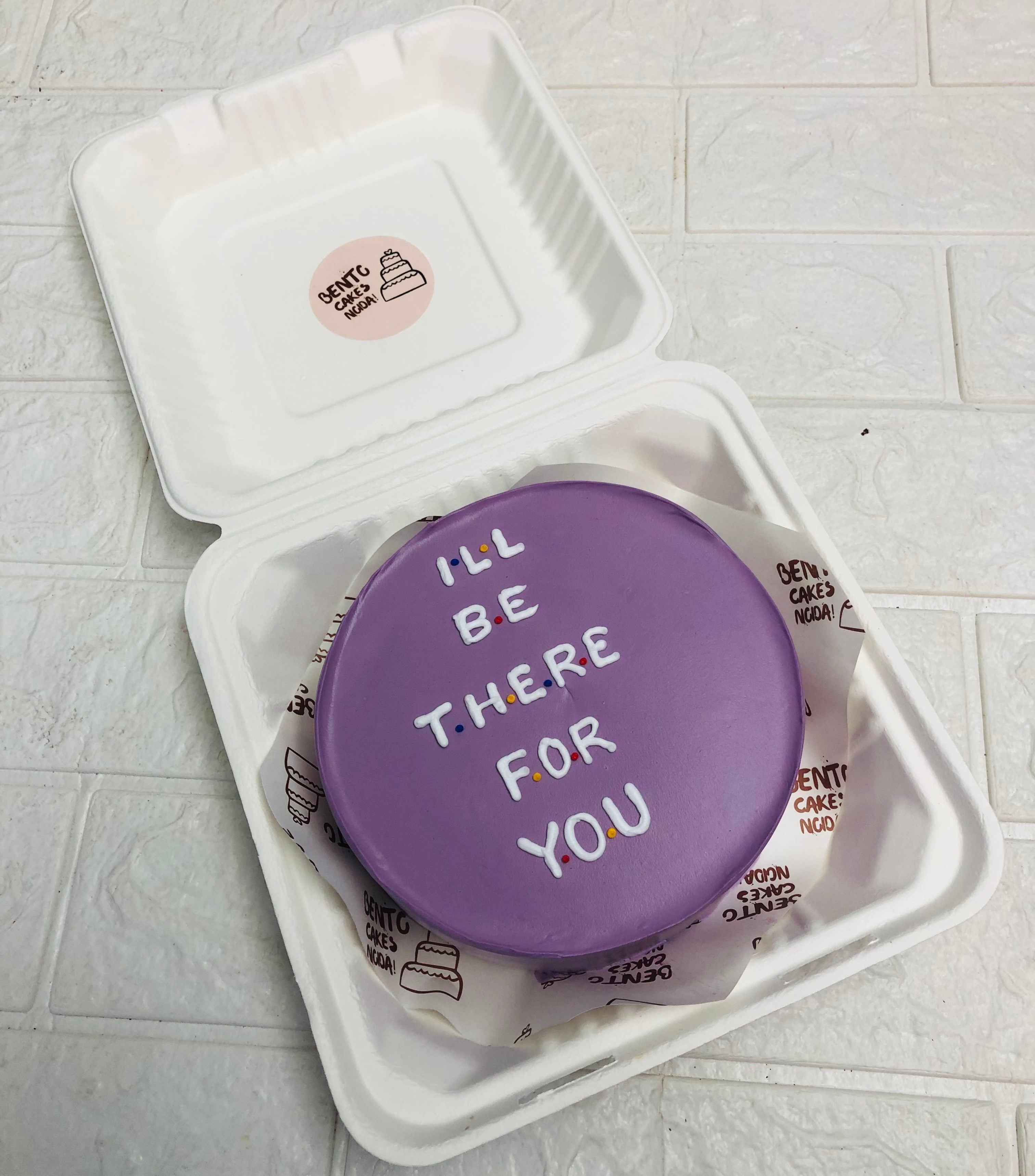 A purple bento cake having a lovely text "I'LL BE THERE FOR YOU" with white icing.
