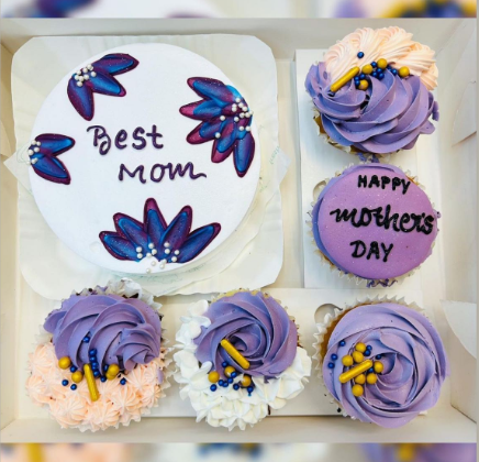 A large bento box containing 1 cake and 5 cupcakes. A blue floral design cake having "Best Mom" text and cupcakes having purple and light pink floral designs.