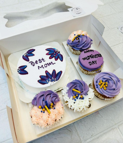 A large bento box containing 1 cake and 5 cupcakes. A blue floral design cake having "Best Mom" text and cupcakes having purple and light pink floral designs.
