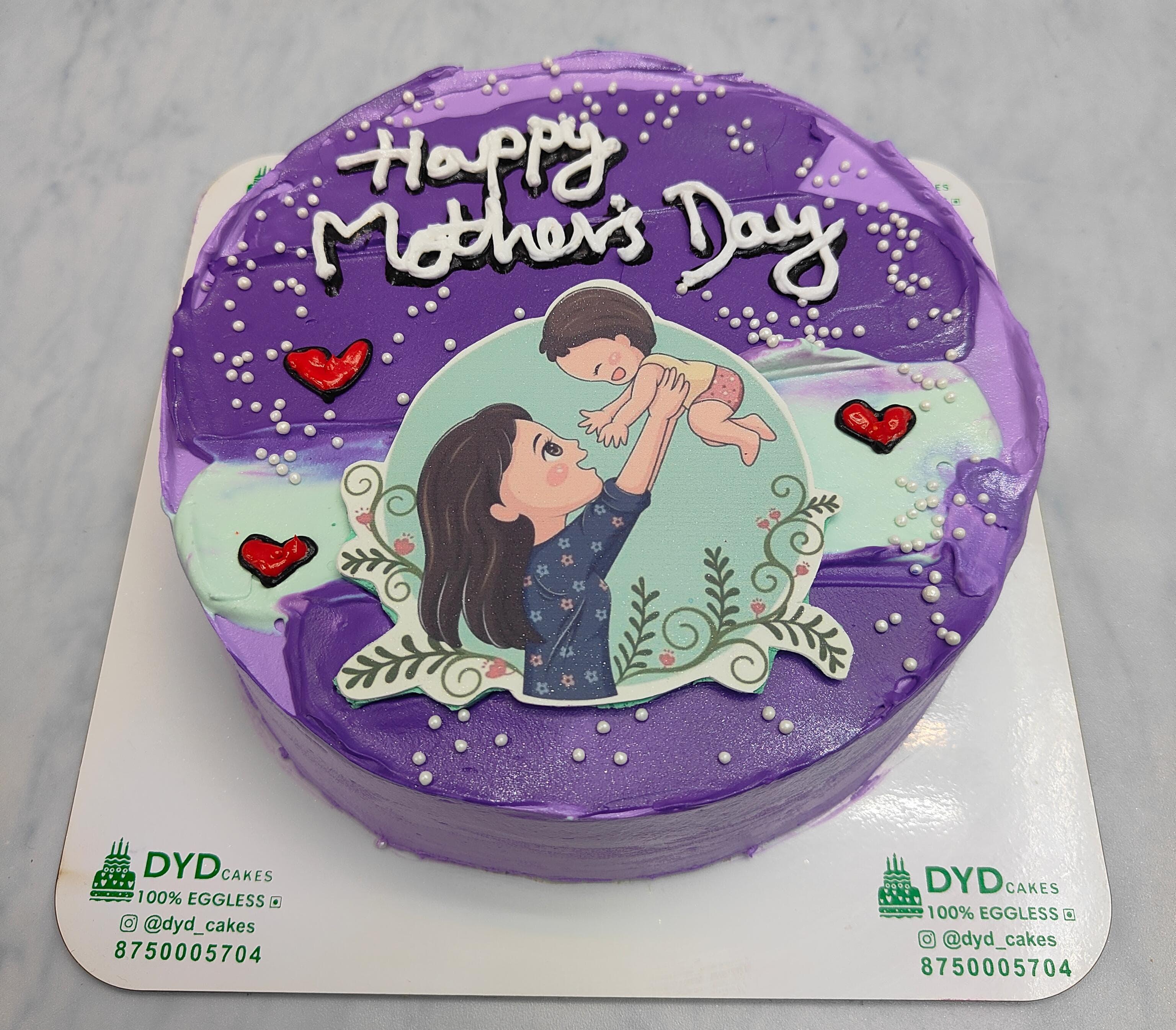 A shiney purple cake with aesthetic shades on it and a mother baby sticker placed on it with pretty red hearts designs.