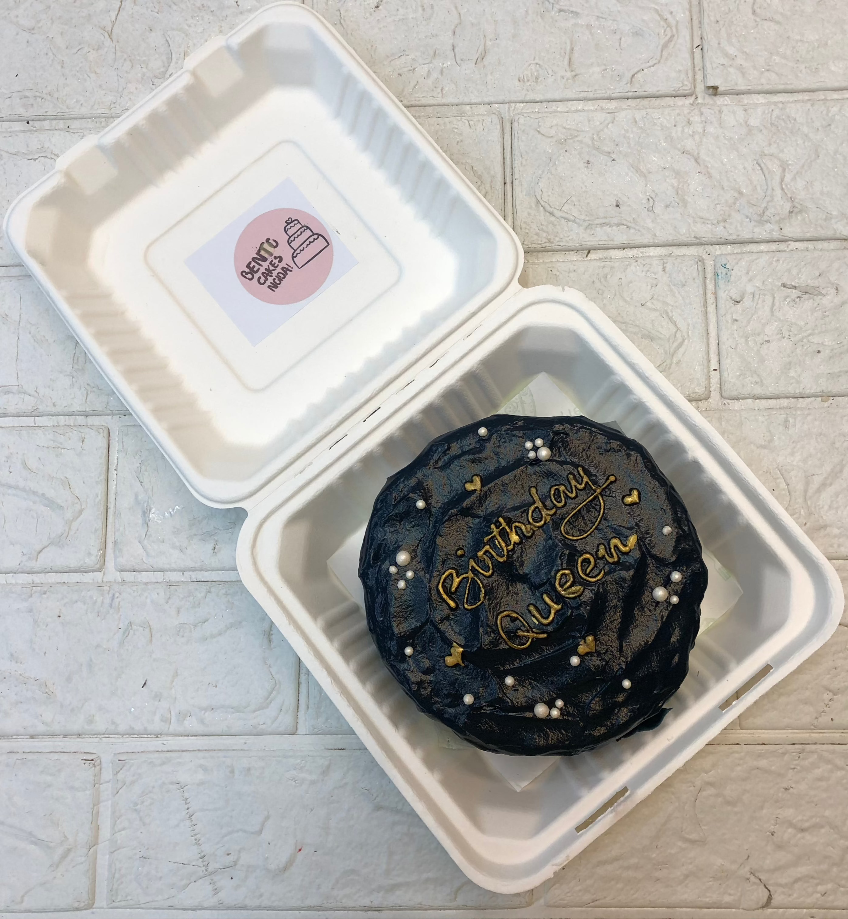 A beautifully decorated birthday cake with white and gold accents, featuring the words "Birthday Queen" written in gold icing.