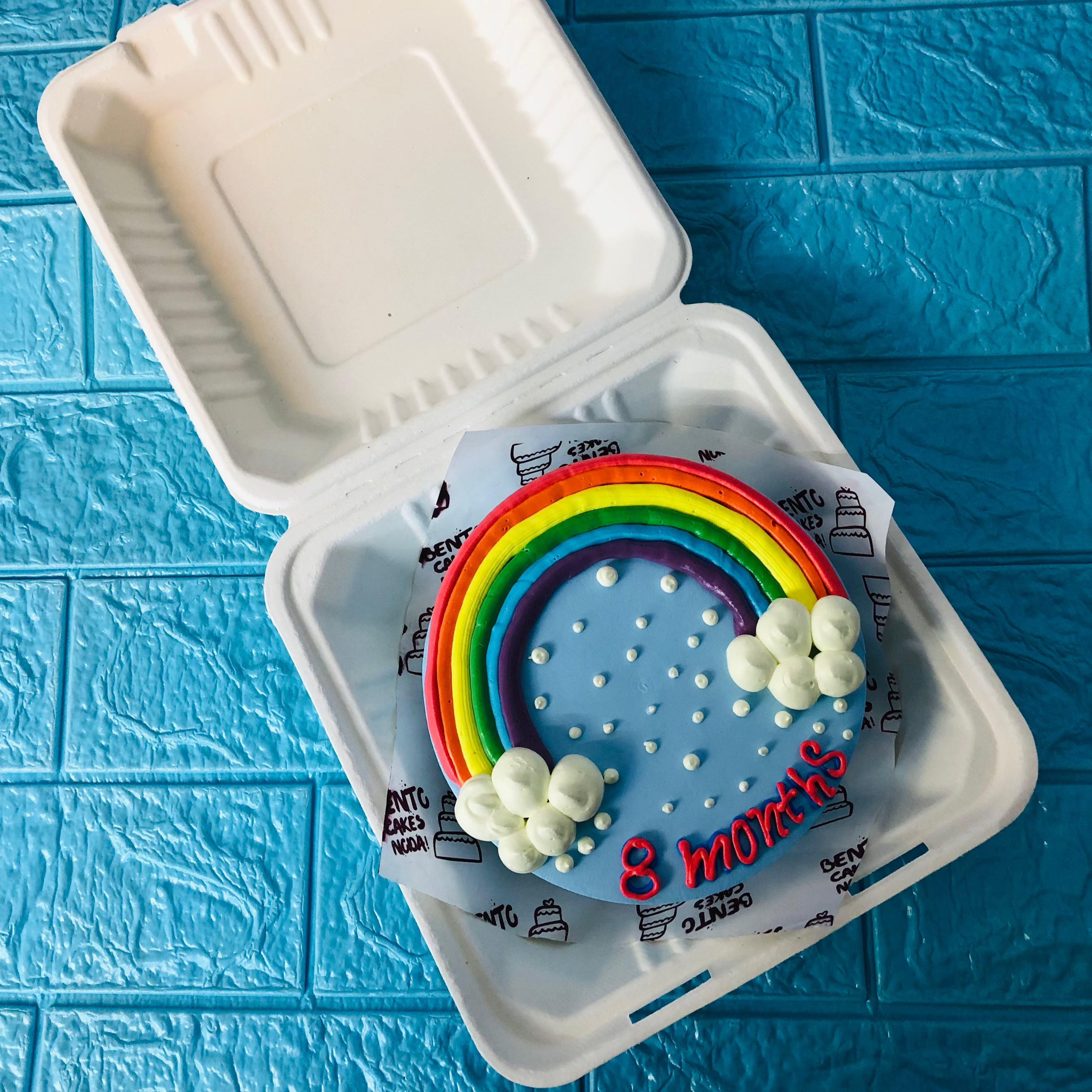A light blue bento cake having rainbow design on it.