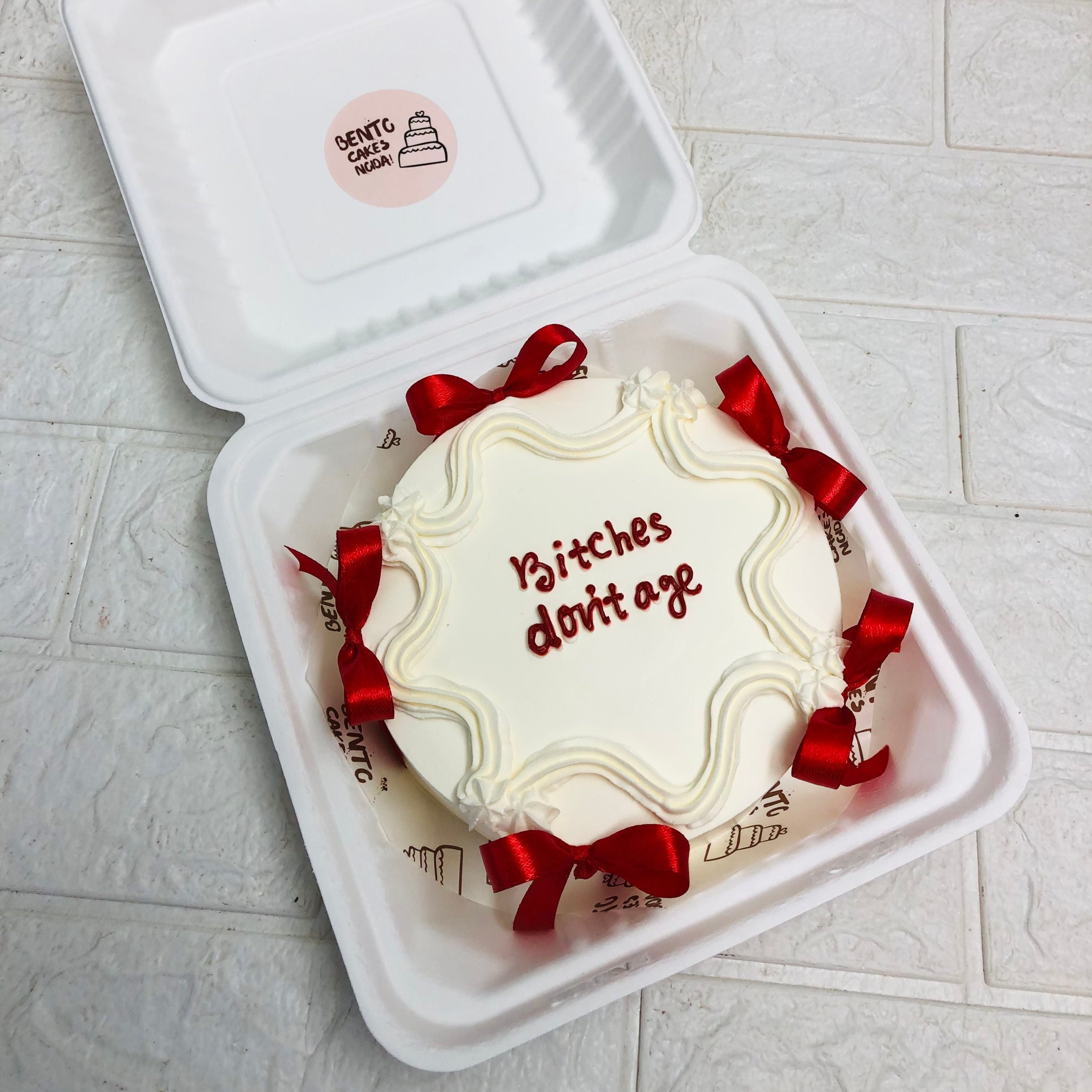 A white bento box adorned with a red bow, featuring a beautifully decorated cake on top.