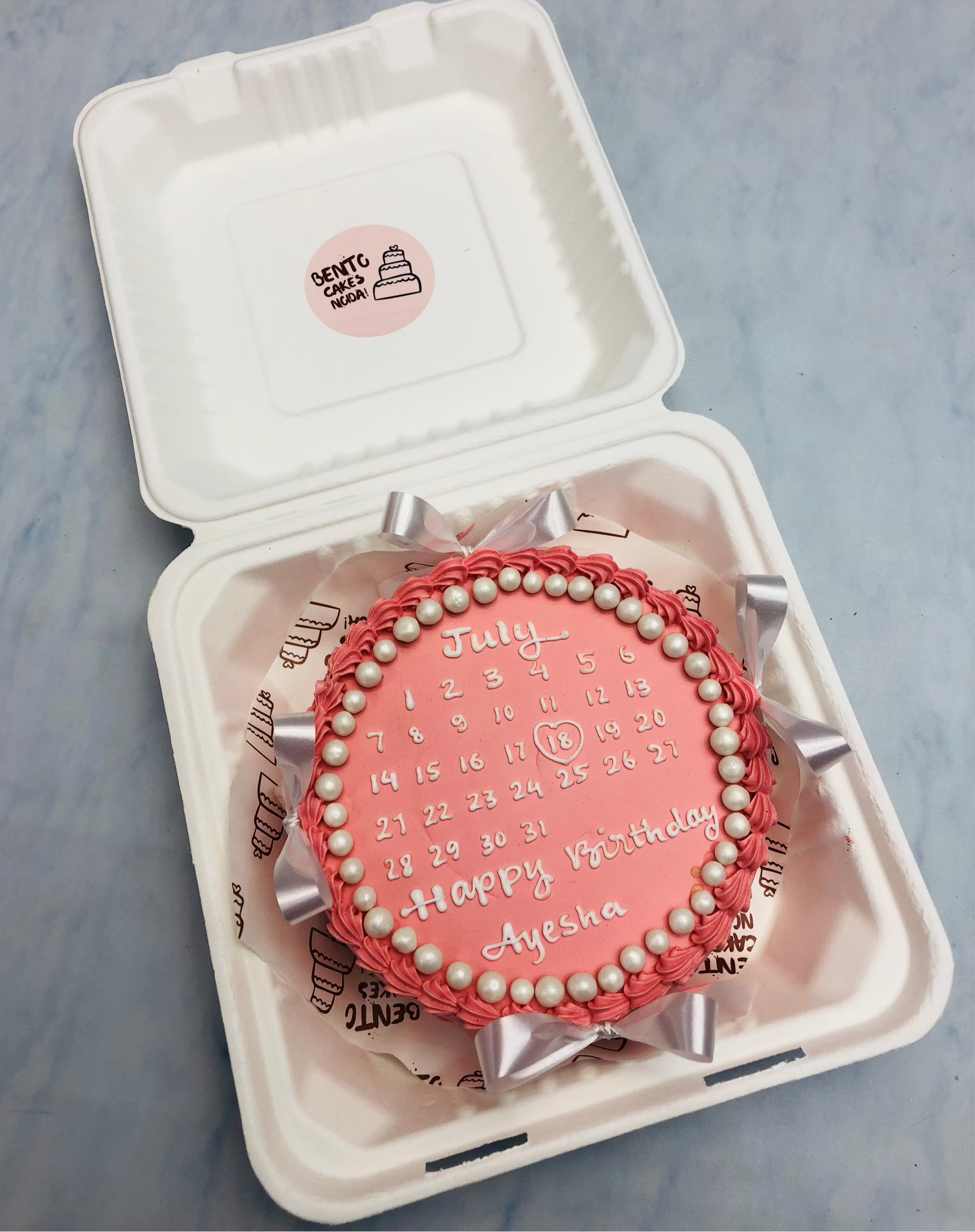 A red color bento cake with white bows and calendar design on it. 