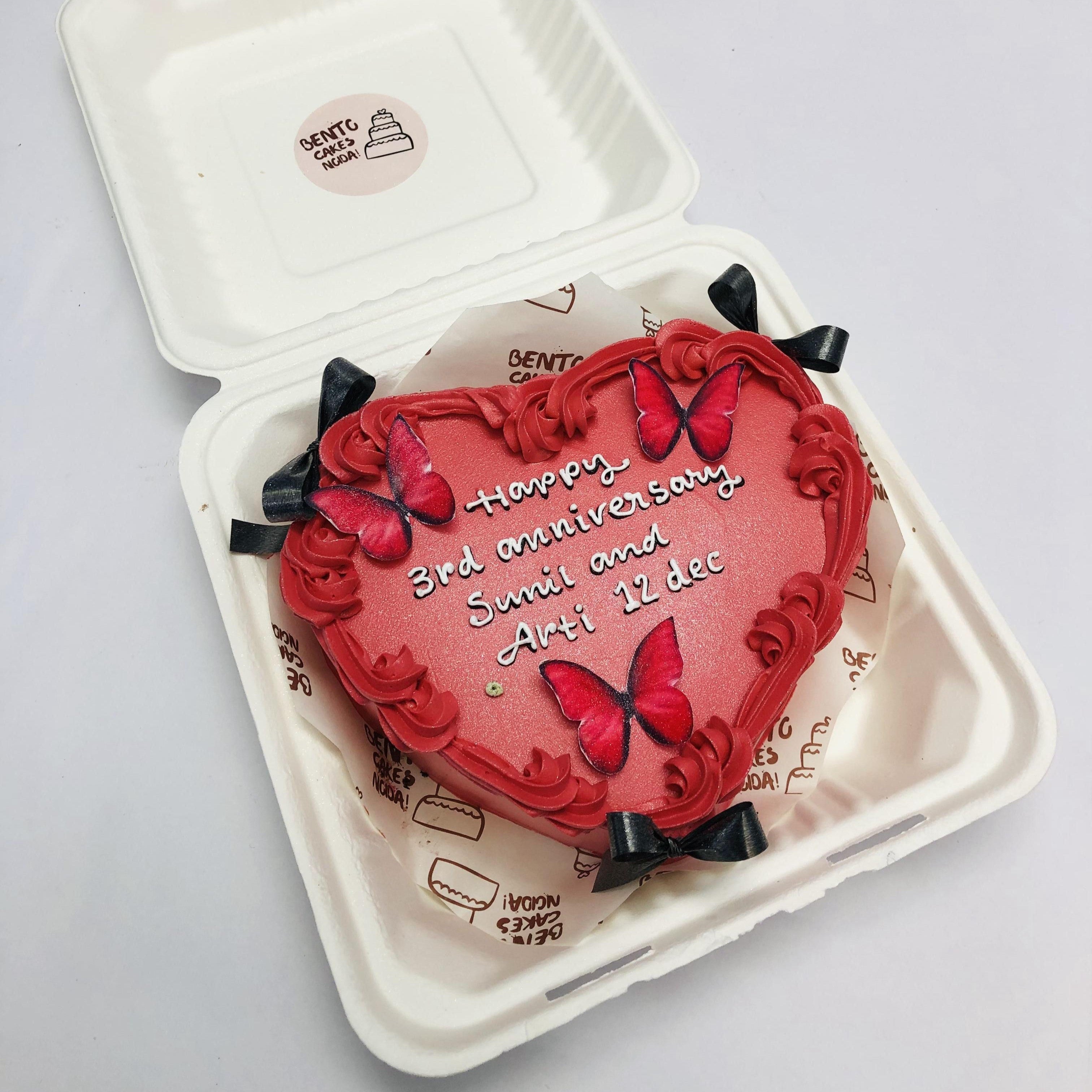 A Dark red heart shape bento cake with red buttefrflirs and decorated with black bow.