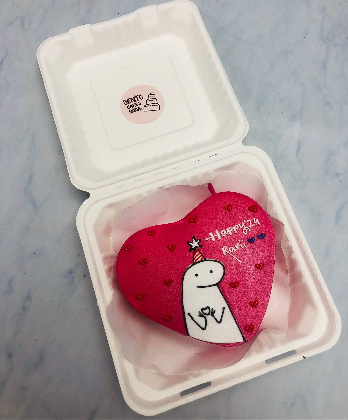 A dark red bento cake in heart shape having a Mimi design on it.