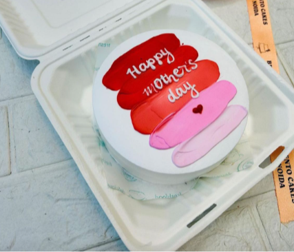 A white cake with red, pink shades on top and a text "Happy Mother's Day" written with whiten icing on it.
