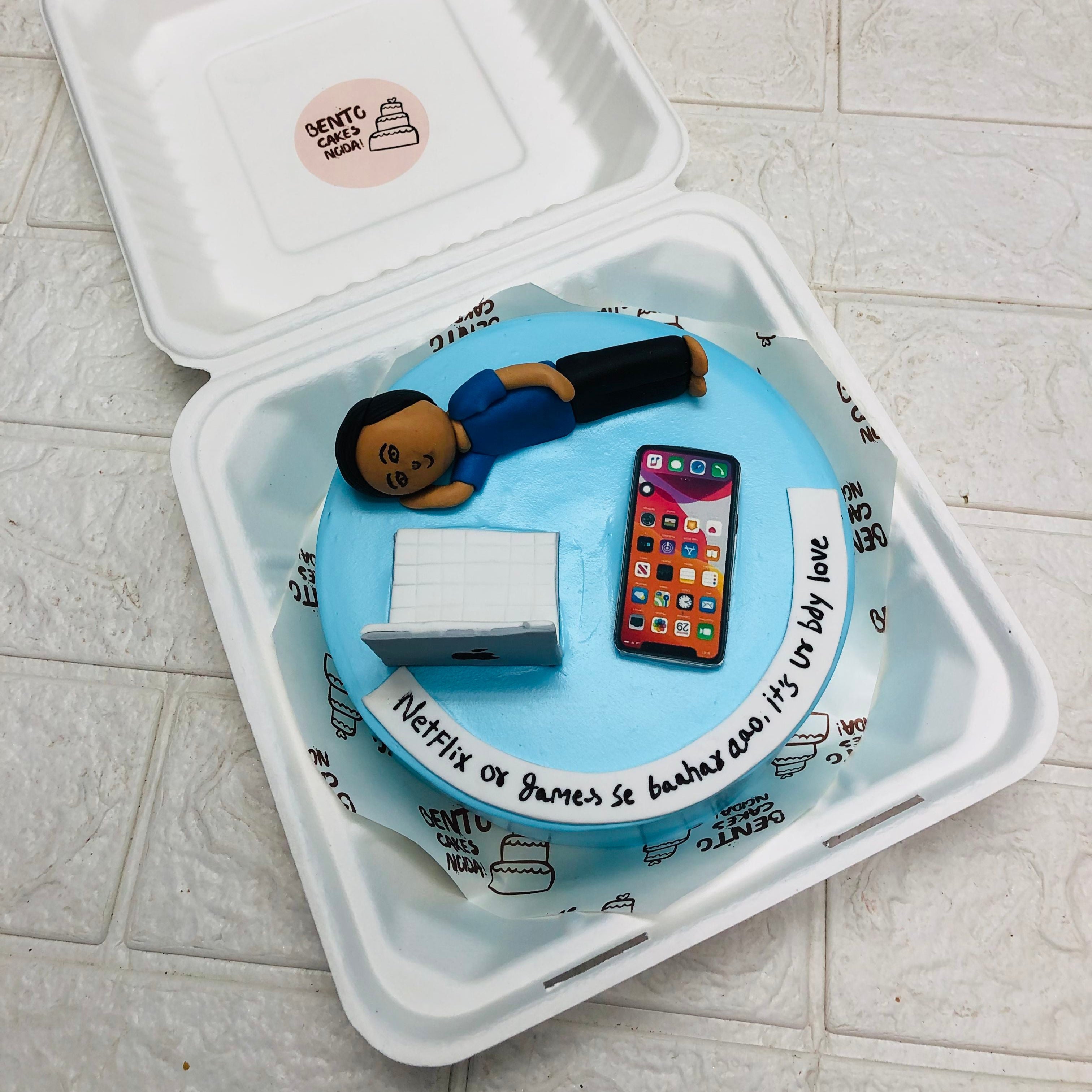 A cake in a box beside a sleepy man resting with his head on the table, creating a cozy, relaxed atmosphere.