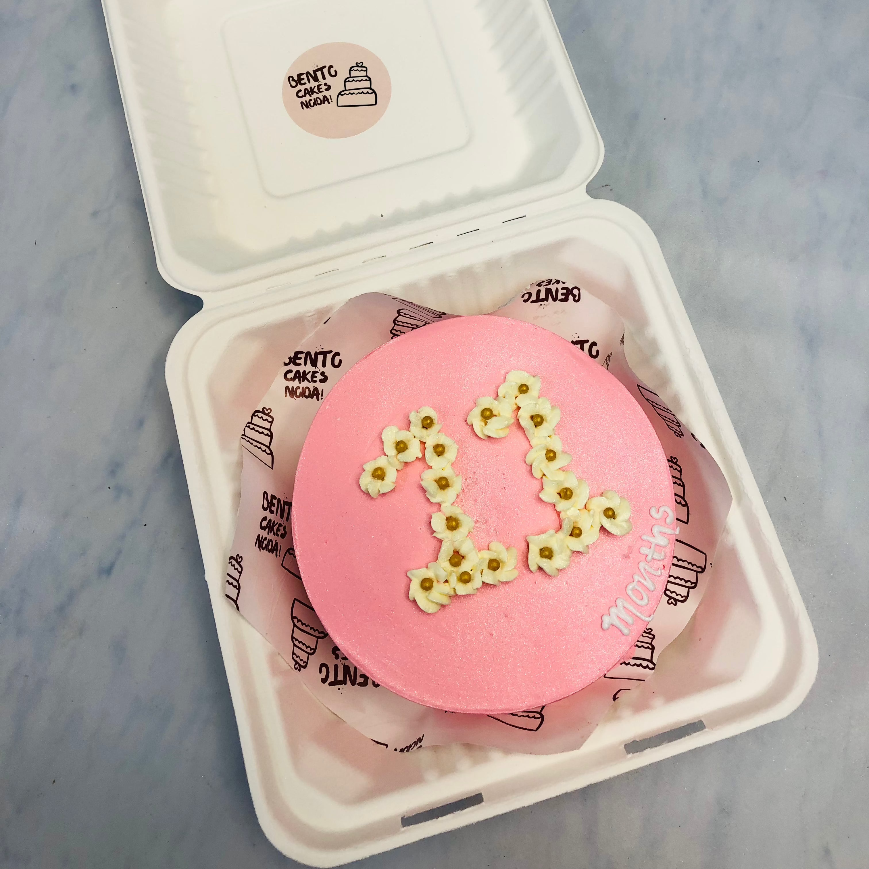 A rose gold color bento cake with "11" written on it.