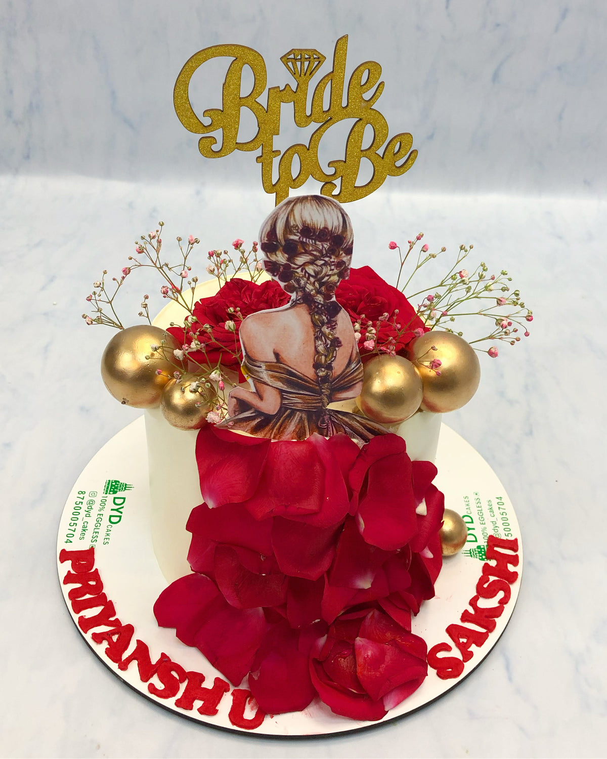 A white bento cake is designed for bride to be with red rosed pattels and golden balls.